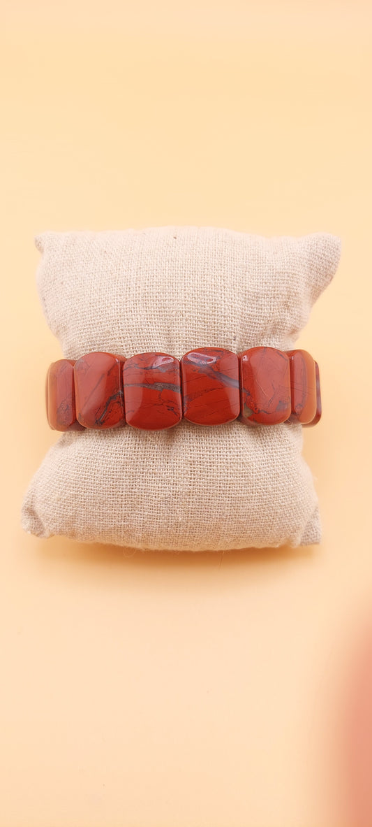 A red jasper soft bangle displayed on a beige cushion against a yellow background.