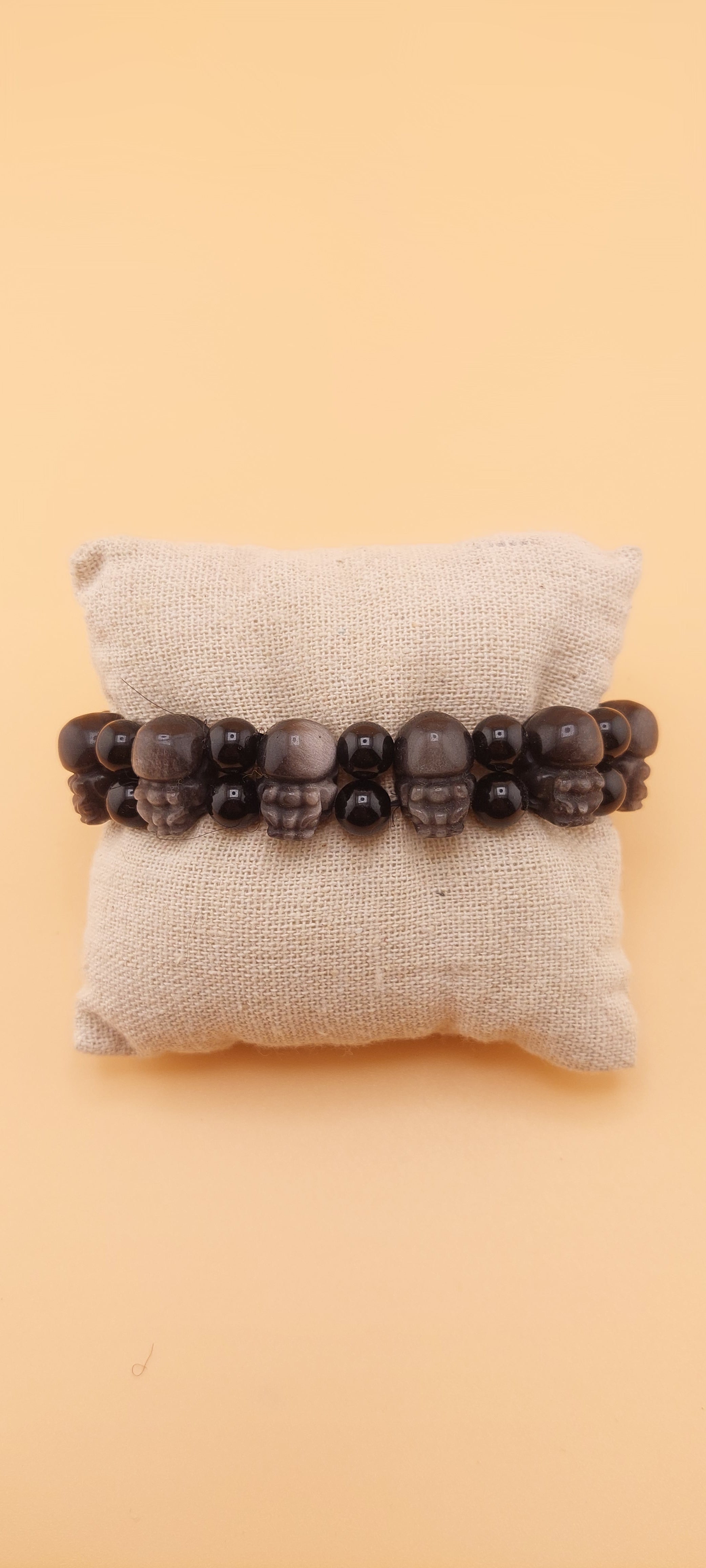 A double bracelet made of black obsidian stones with a silver pixiu design, displayed on a white cushion.