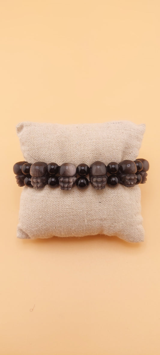 A double bracelet made of black obsidian stones with a silver pixiu design, displayed on a white cushion.