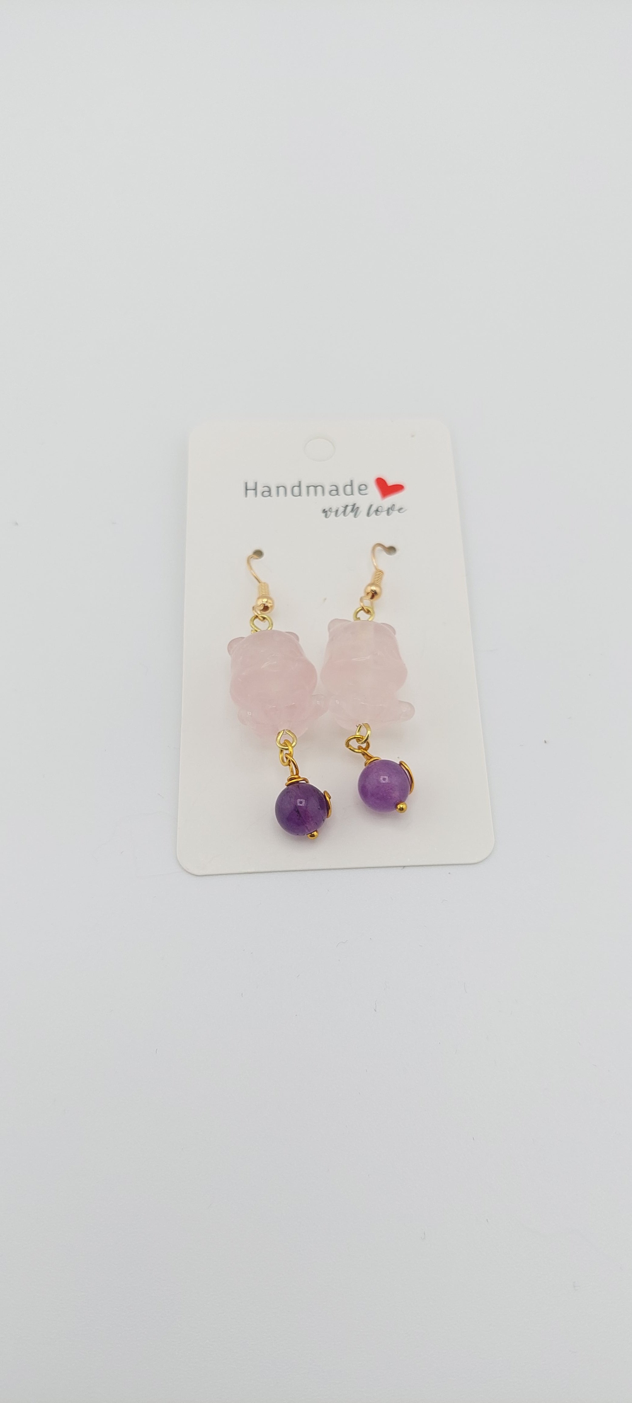 A pair of rose quartz earrings with a design resembling Winnie the Pooh, displayed on a white card with the brand name 'Jade Couture' at the top.