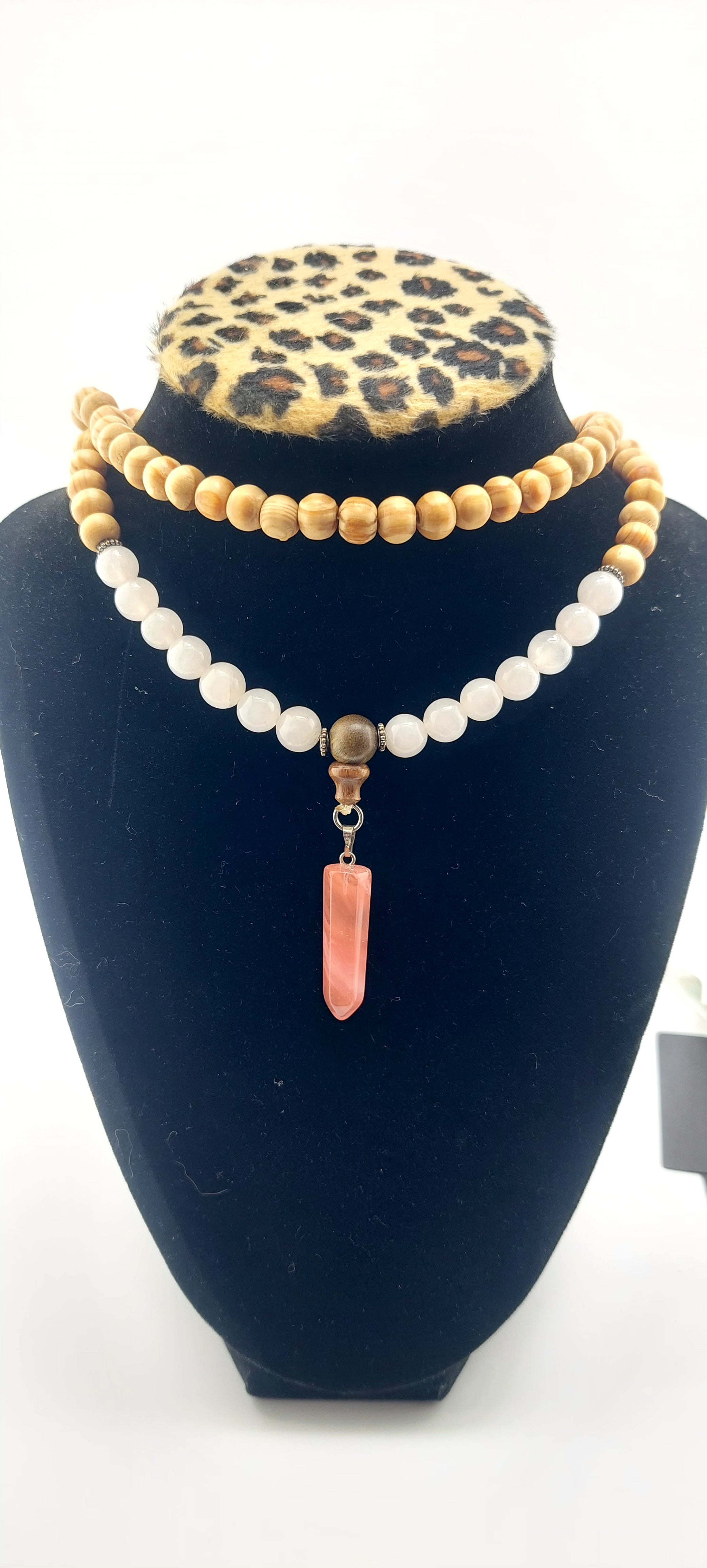 A two-strand necklace made of wood and white jade, featuring a pink pendant, displayed on a mannequin's neck.