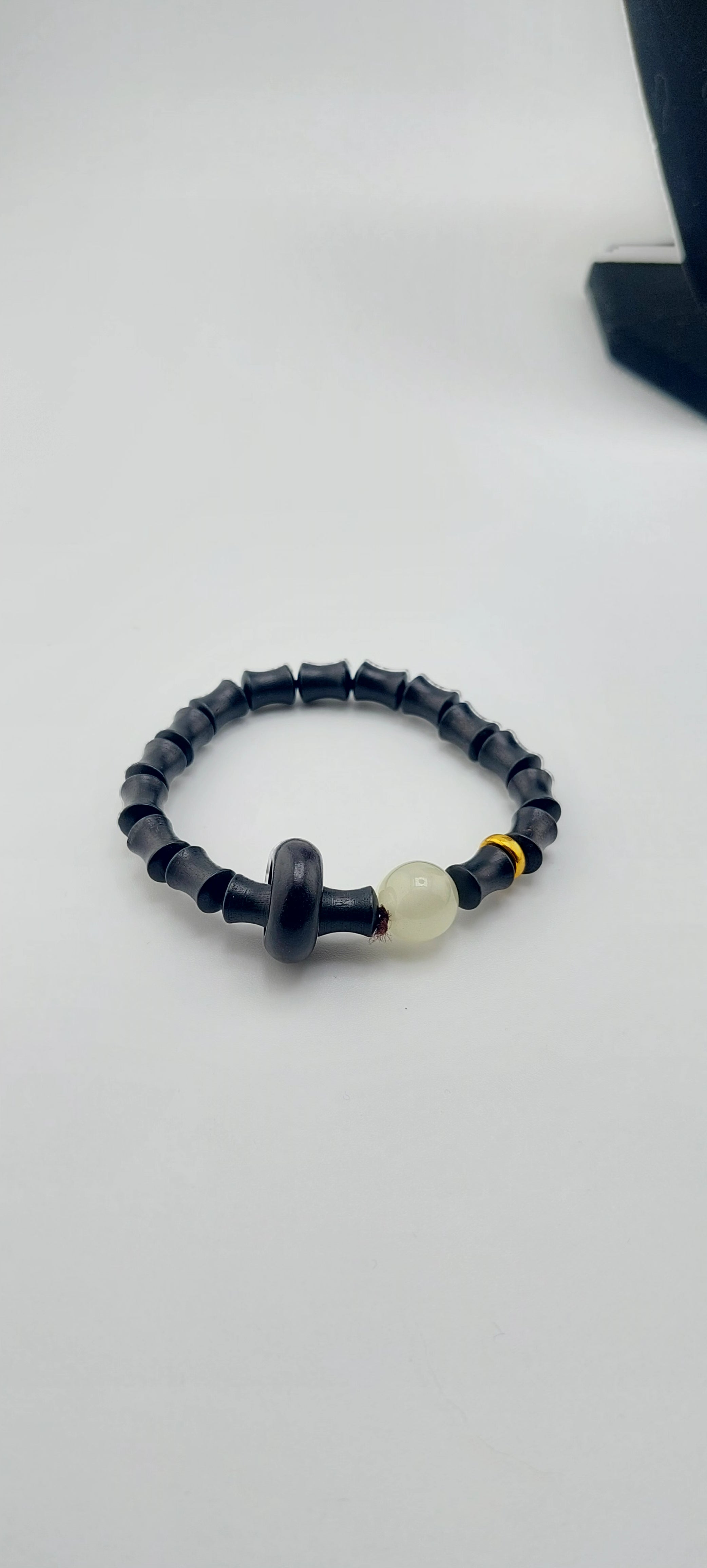 A bamboo wood bracelet with a black and white beaded design, featuring a glowing bead, displayed against a white background.