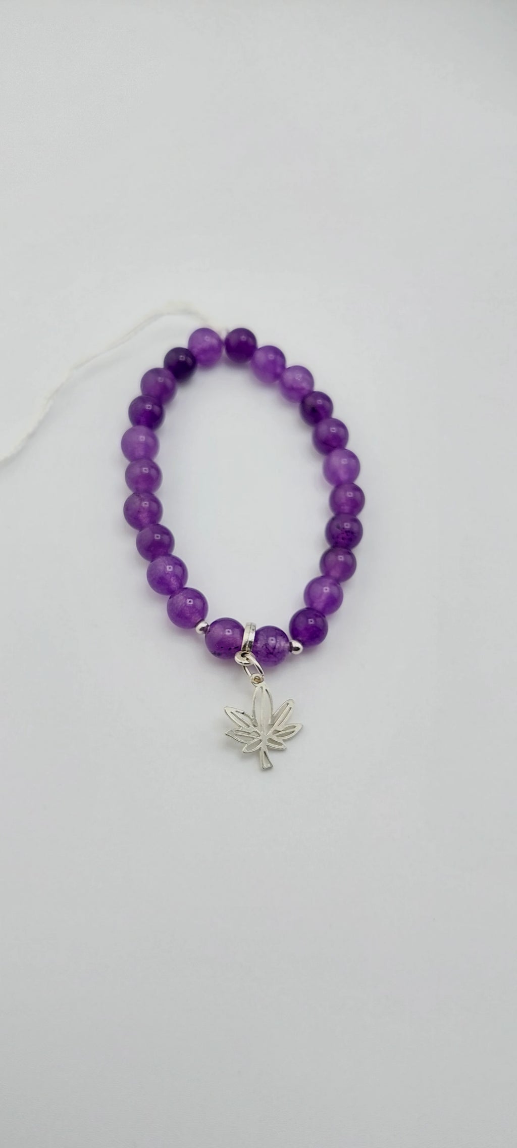 Purple beaded bracelet with a silver leaf charm on a white background
