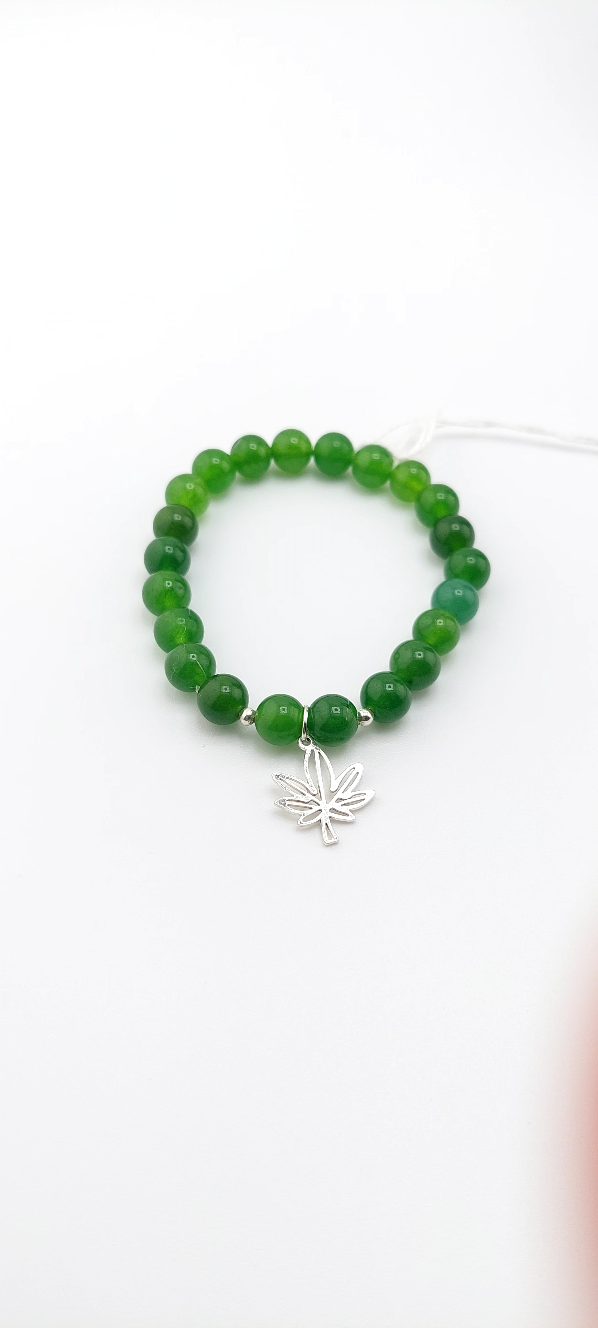 Green beaded bracelet with a silver leaf charm on a white background