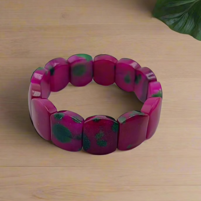 Pink bracelet with green accents on a wooden surface