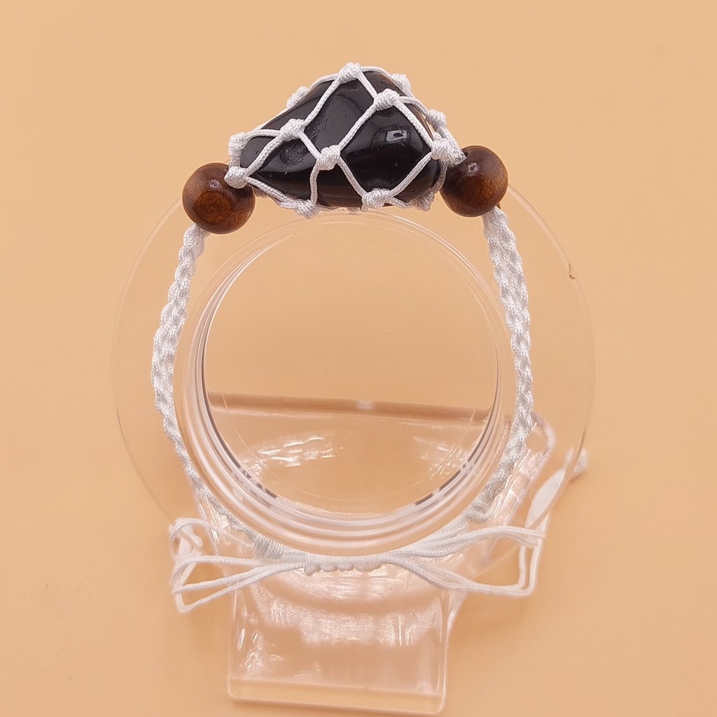 A white Macrame tumbled stone bracelet displayed on a clear stand against a beige background.