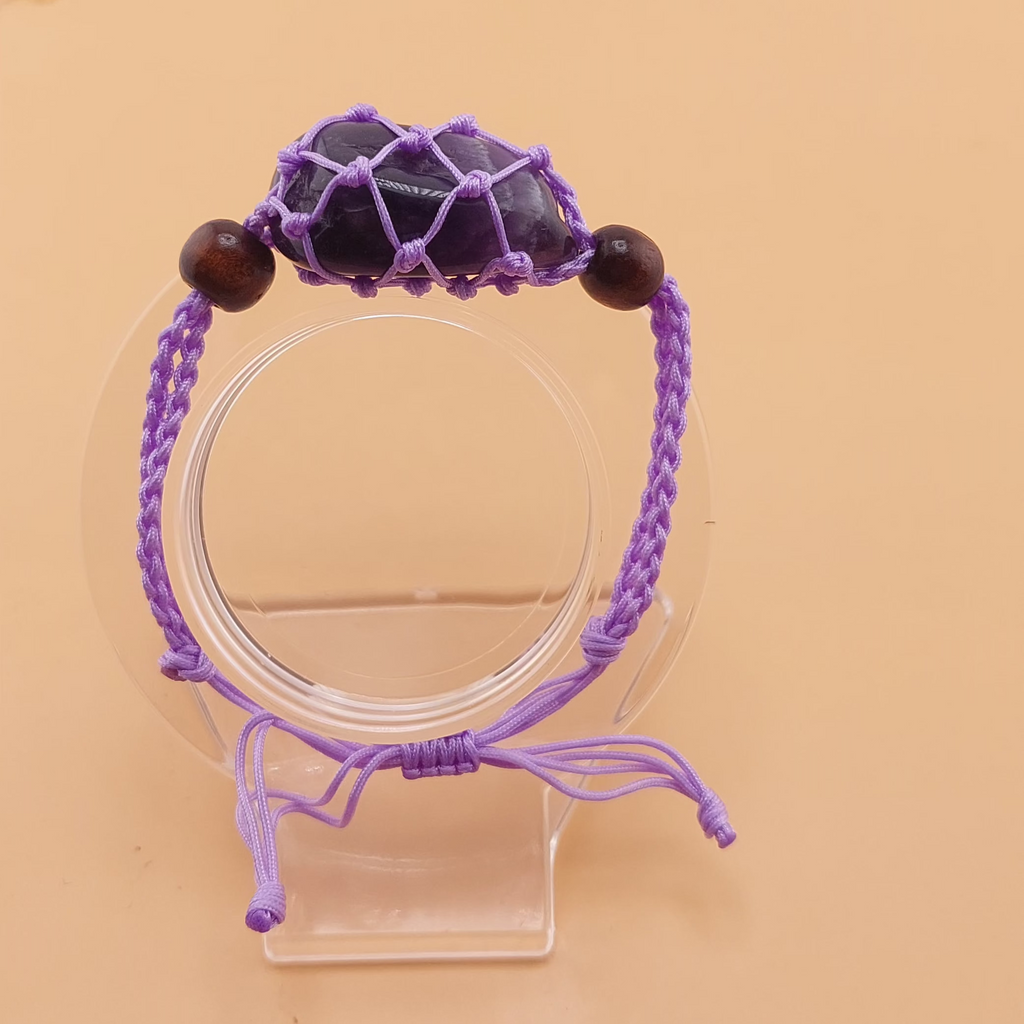 A purple Macrame tumbled stone bracelet displayed on a clear stand against a beige background.