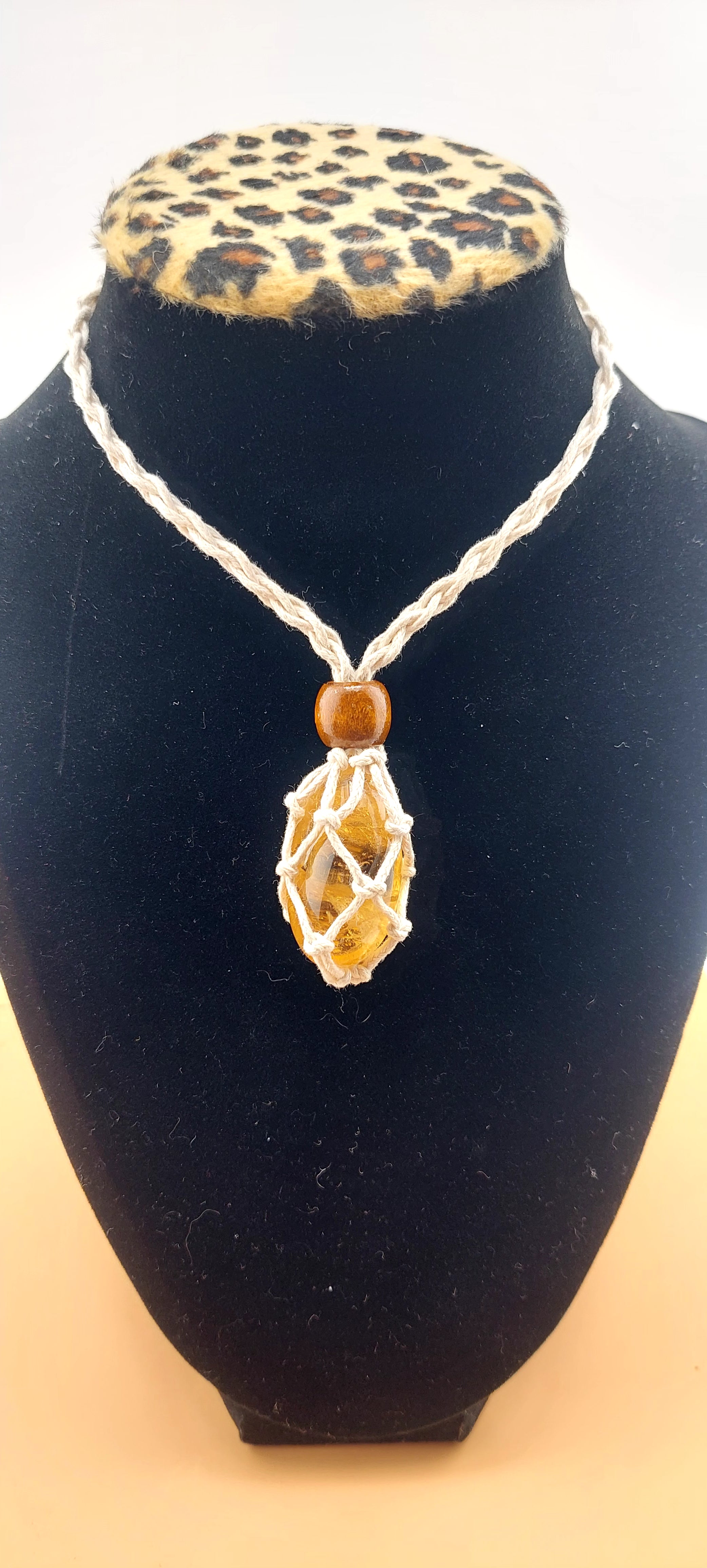 A black macrame necklace with a tumbled stone pendant displayed on a mannequin bust with a leopard print collar.