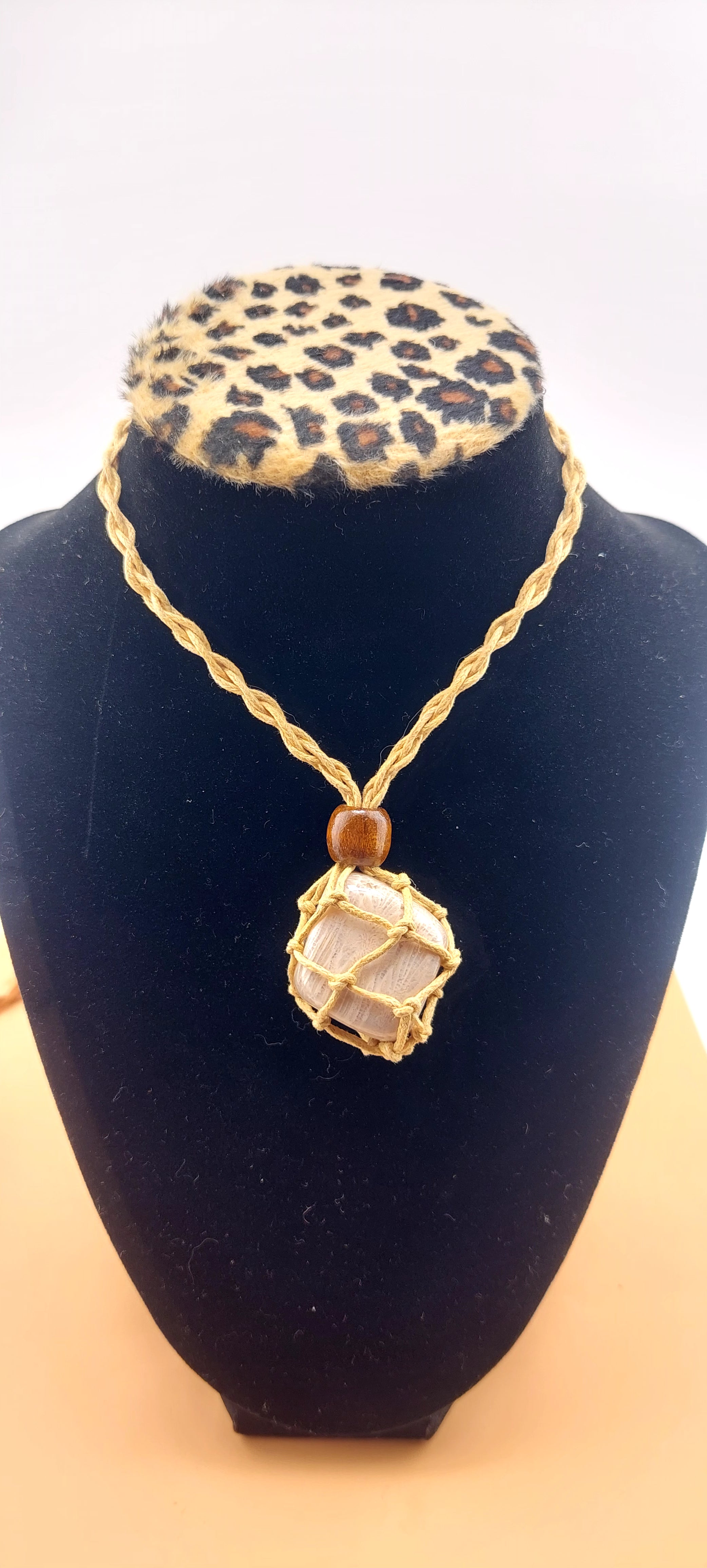 A black macrame necklace with a tumbled stone pendant displayed on a mannequin bust with a leopard print collar.
