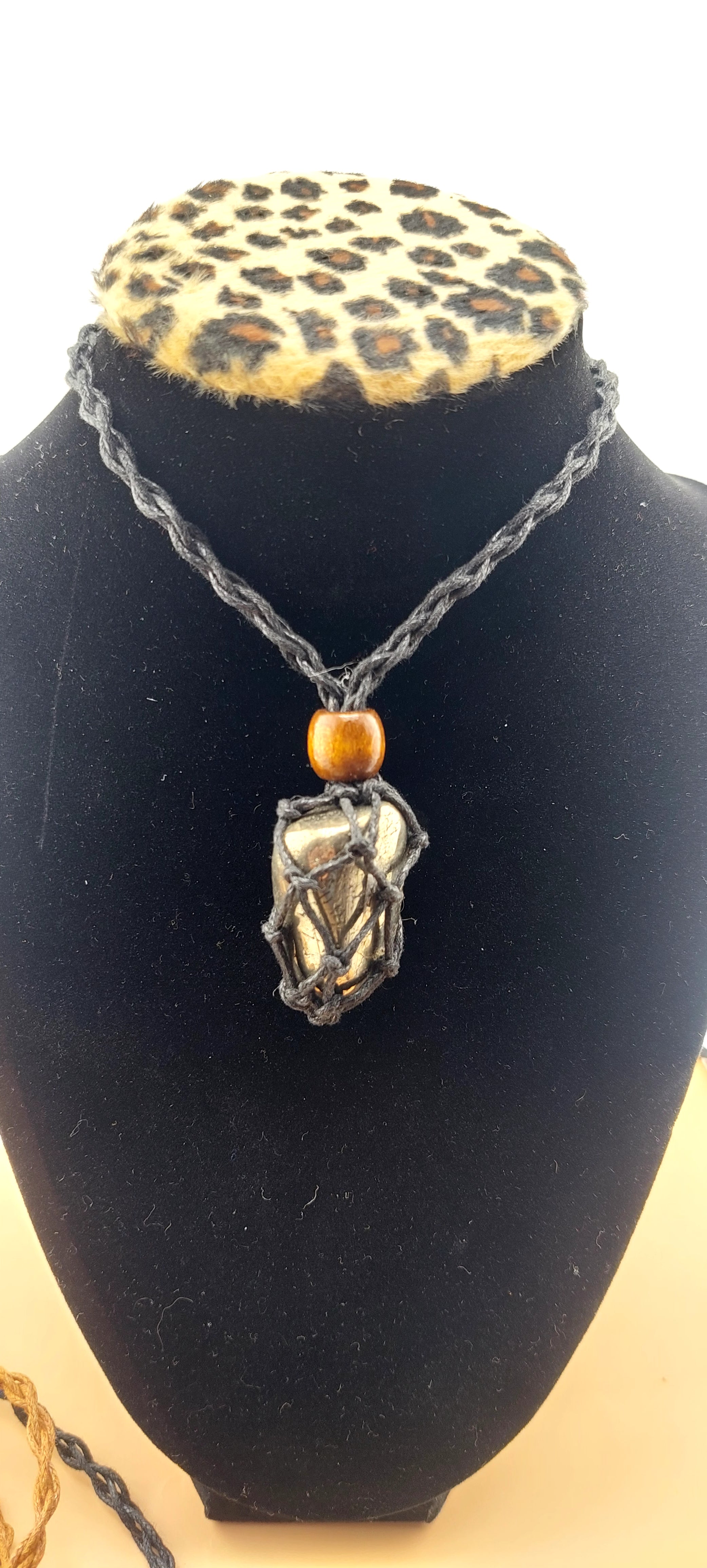 A black macrame necklace with a tumbled stone pendant displayed on a mannequin bust with a leopard print collar.