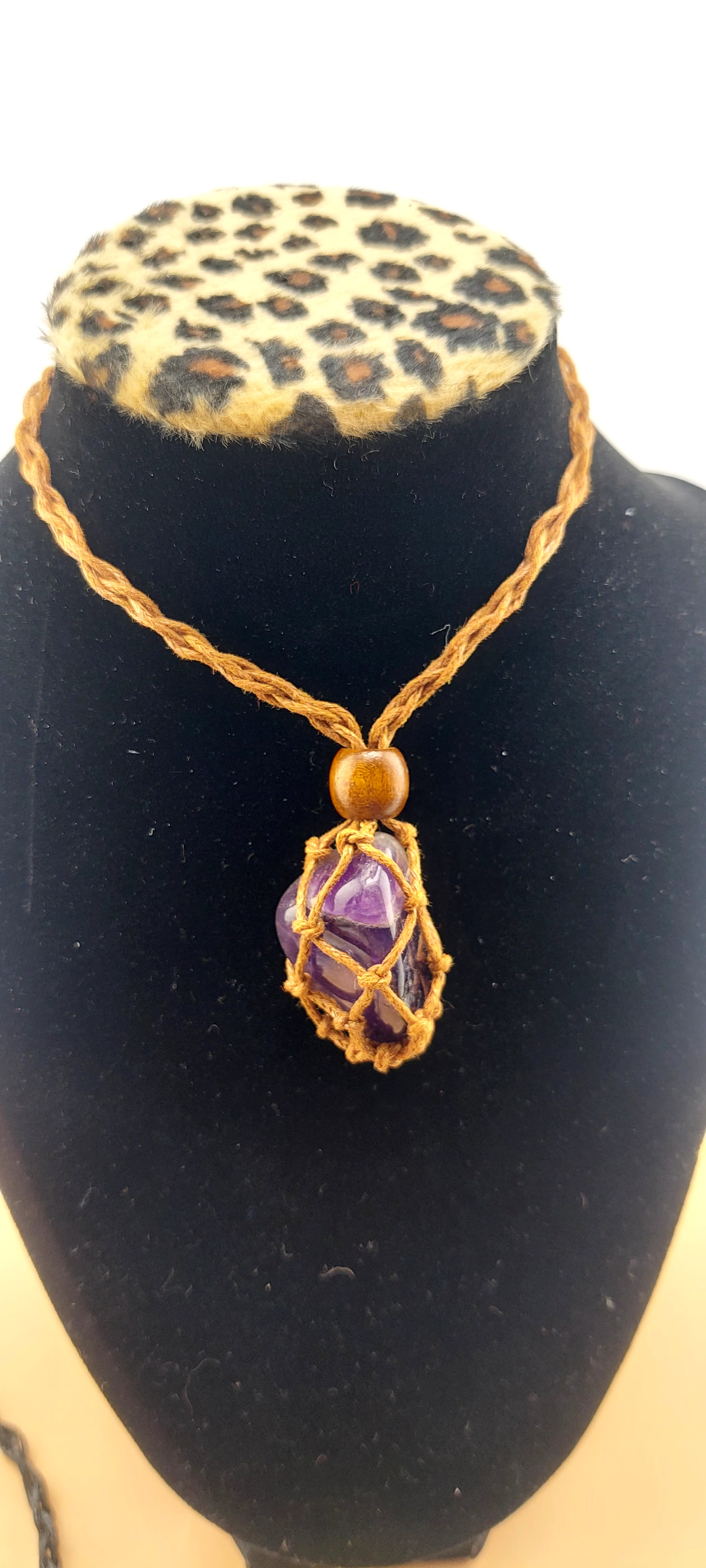 A black macrame necklace with a tumbled stone pendant displayed on a mannequin bust with a leopard print collar.