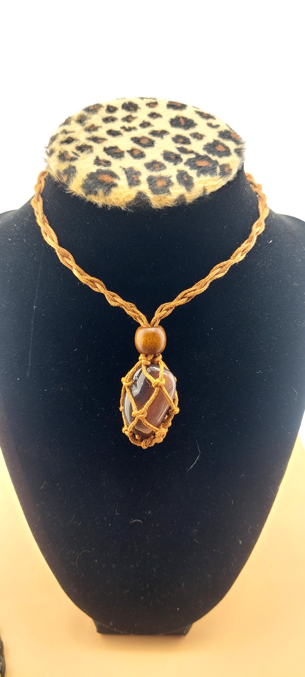 A black macrame necklace with a tumbled stone pendant displayed on a mannequin bust with a leopard print collar.