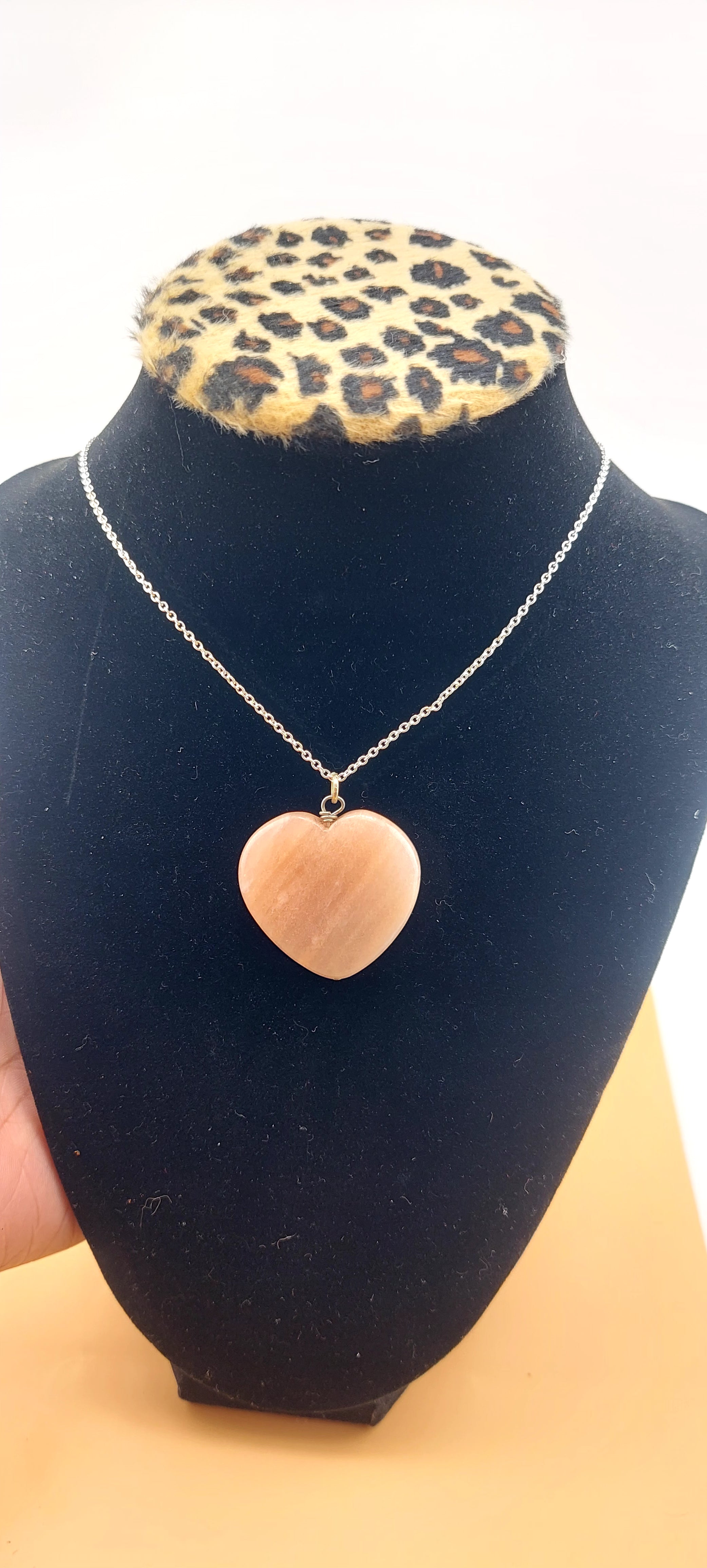 A pink heart-shaped necklace displayed on a black mannequin with a leopard print collar.