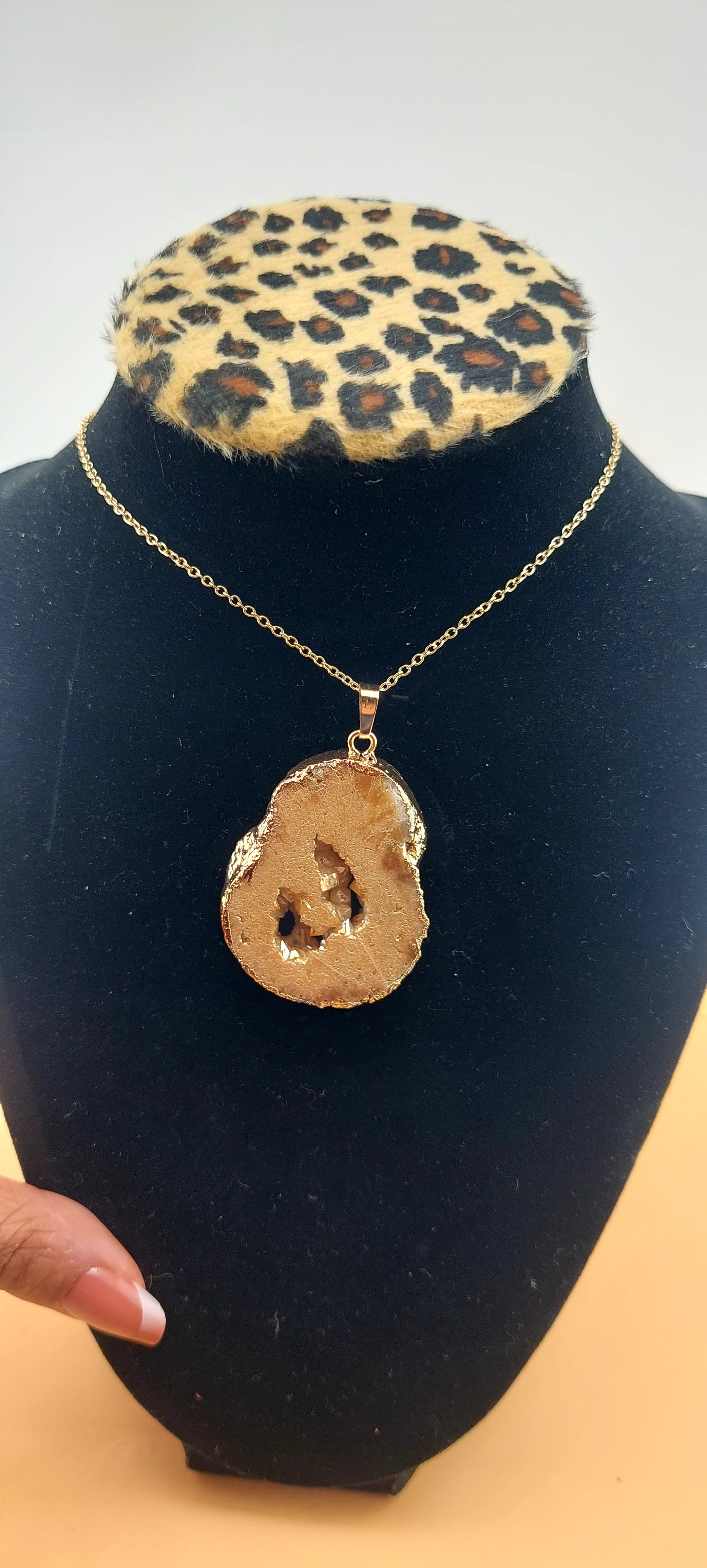 A gold druzy necklace displayed on a black mannequin with a leopard print collar.
