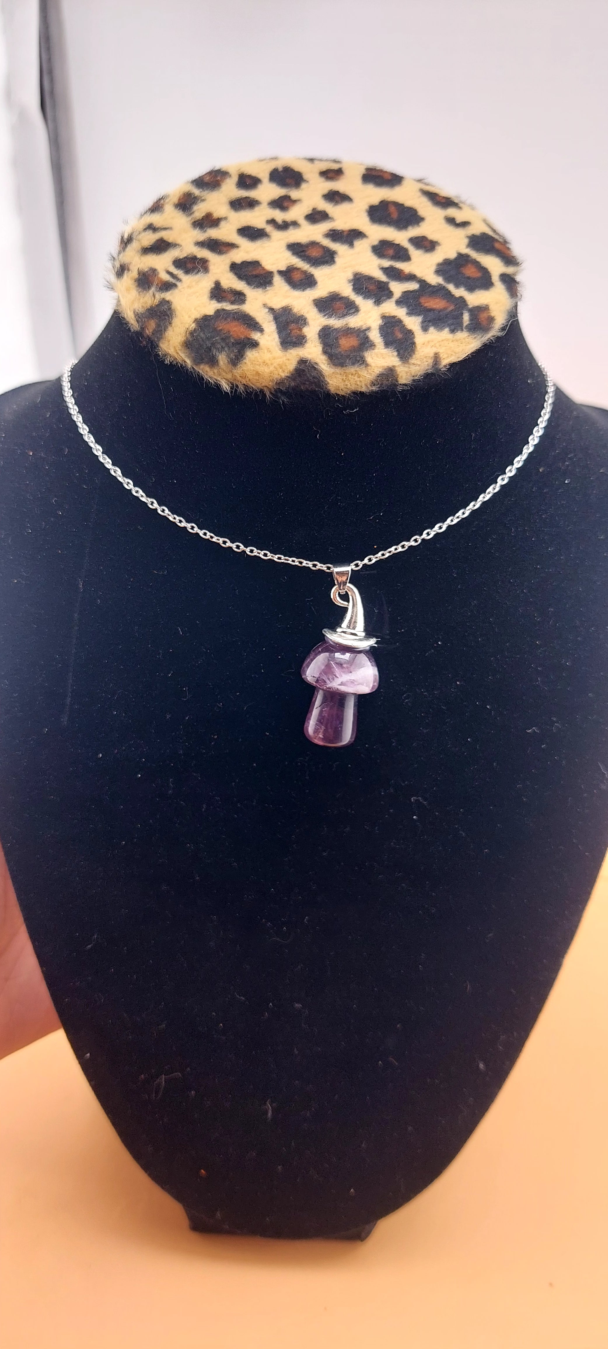 An Amethyst Witch Mushroom Necklace displayed on a black mannequin with a leopard print collar.