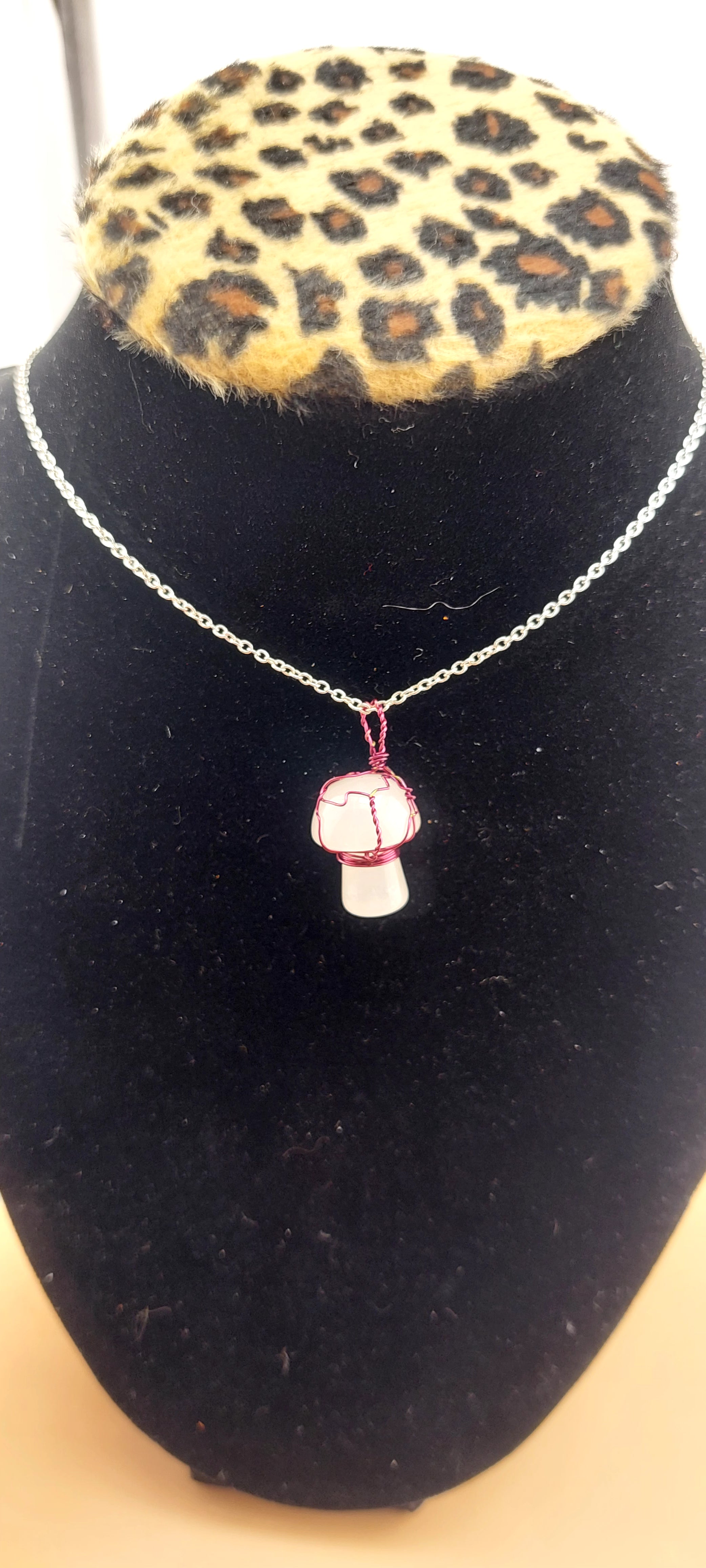 A necklace with a clear quartz mushroom-shaped pendant on a chain, displayed on a black mount with a leopard print base.