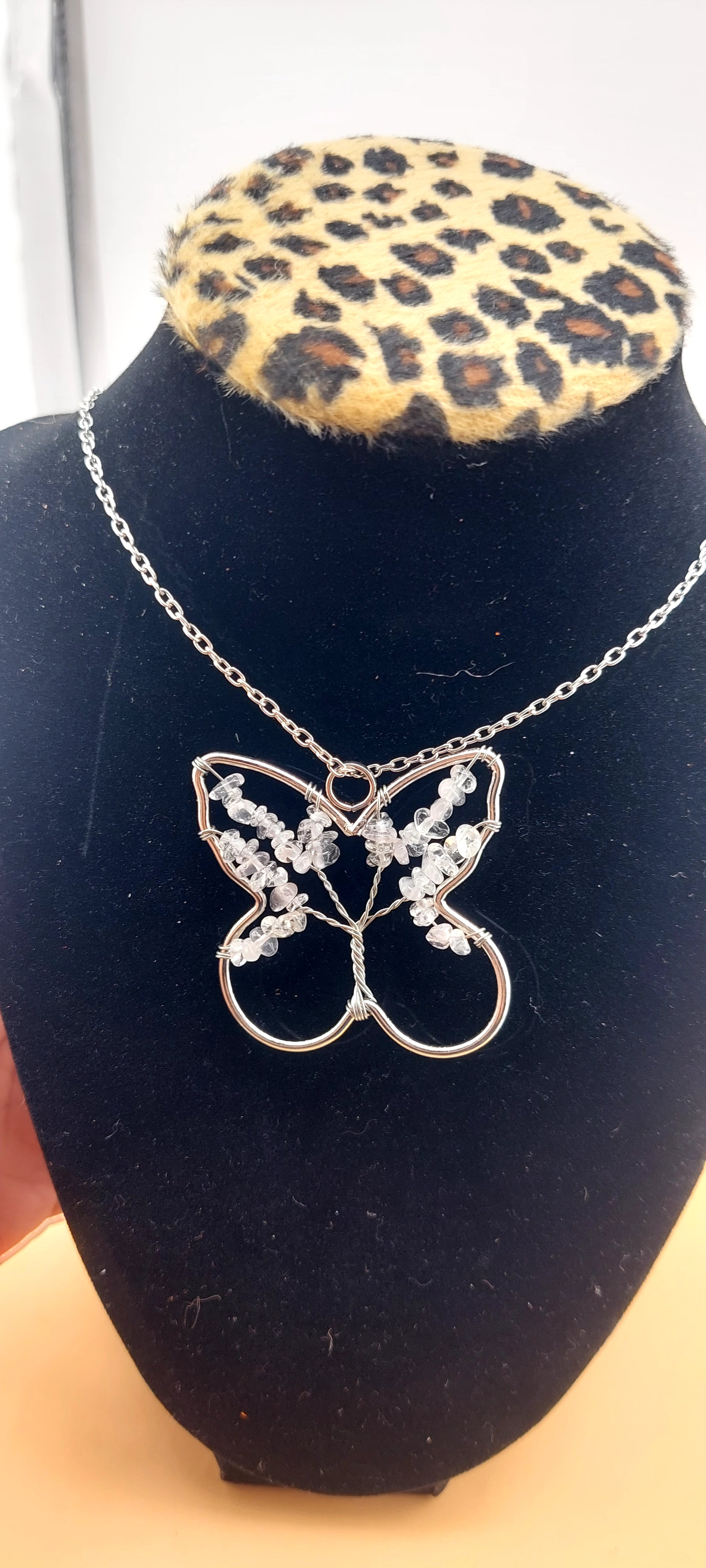 A clear quartz necklace with a butterfly-shaped pendant, displayed on a black stand with a leopard print base.