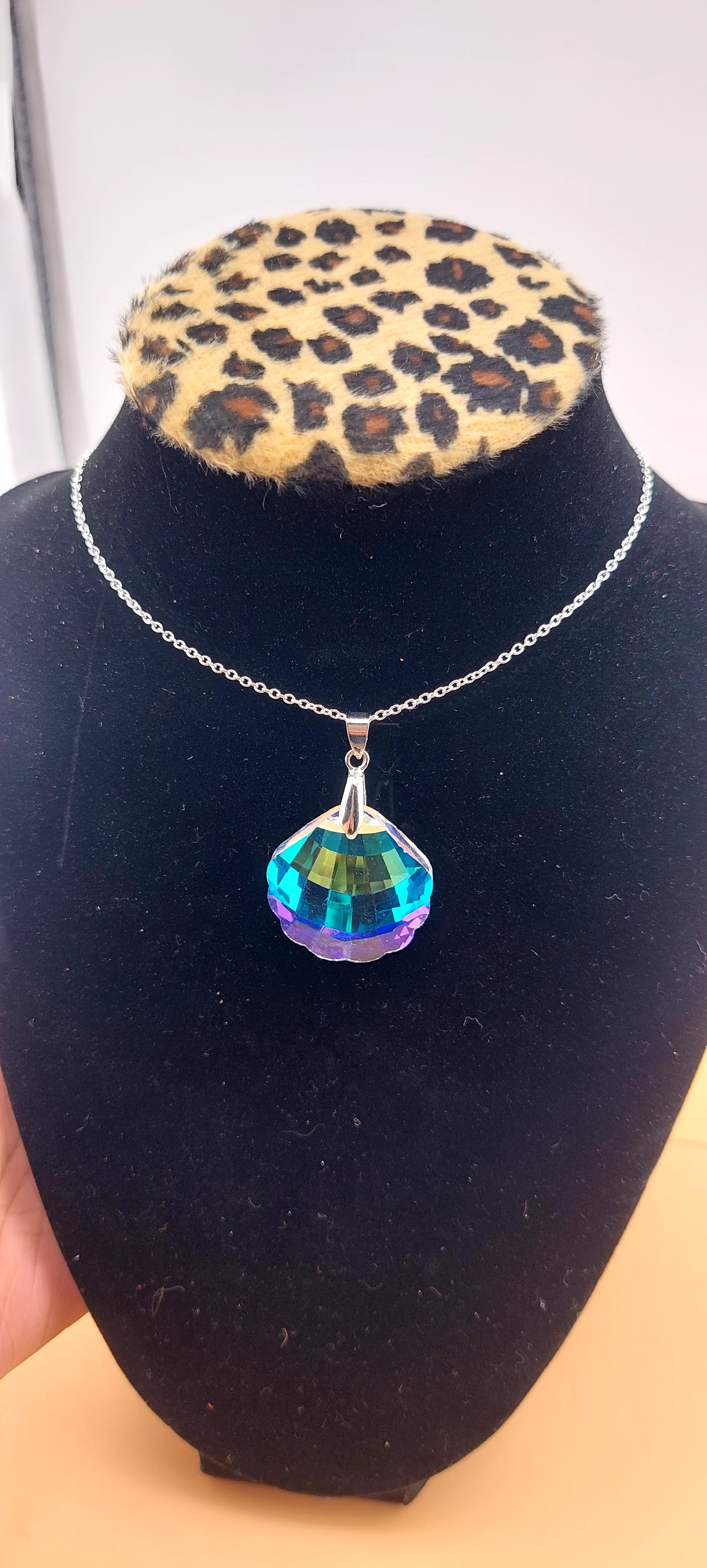 A multicolored glass clam-shaped necklace displayed on a black mannequin with a leopard print collar.