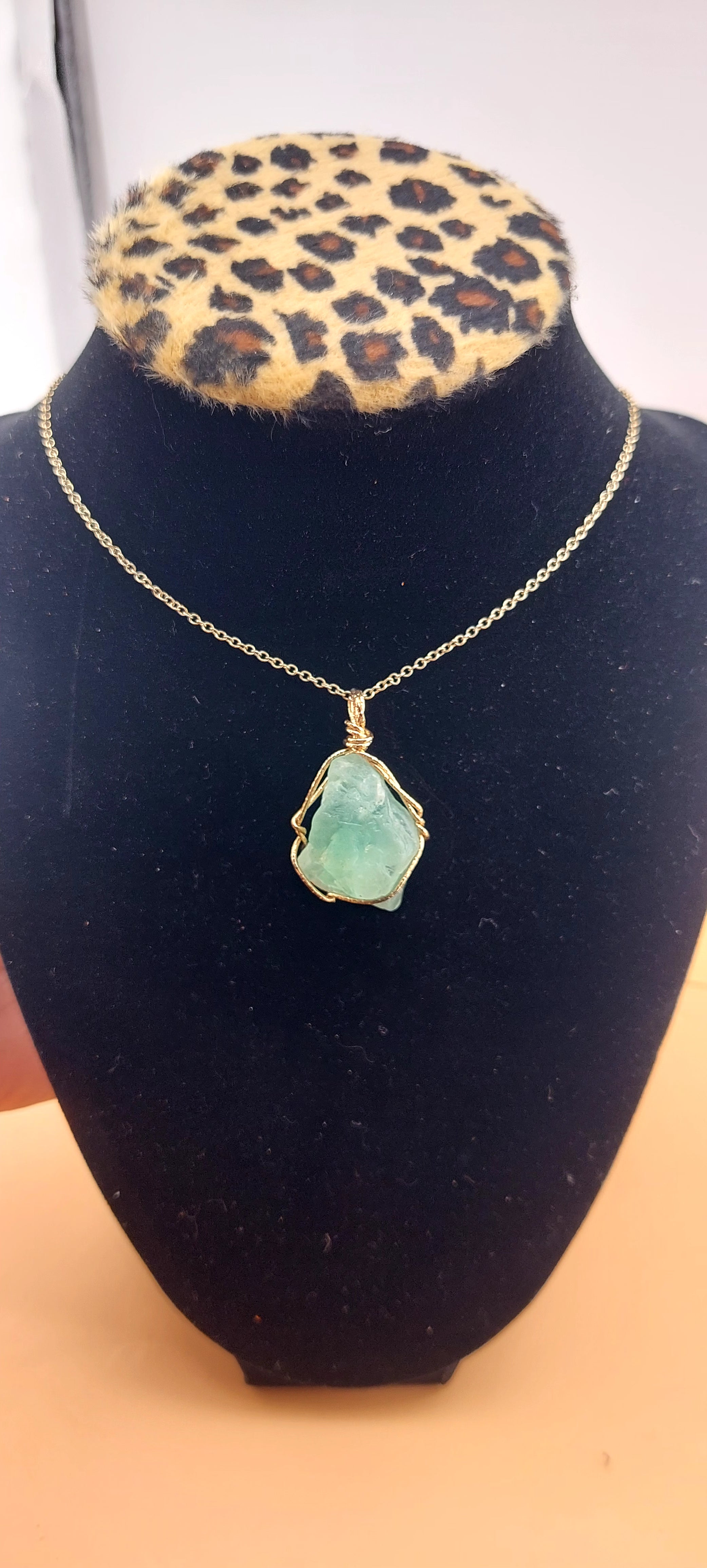 A green adventurine necklace displayed on a black mount with a leopard print background.