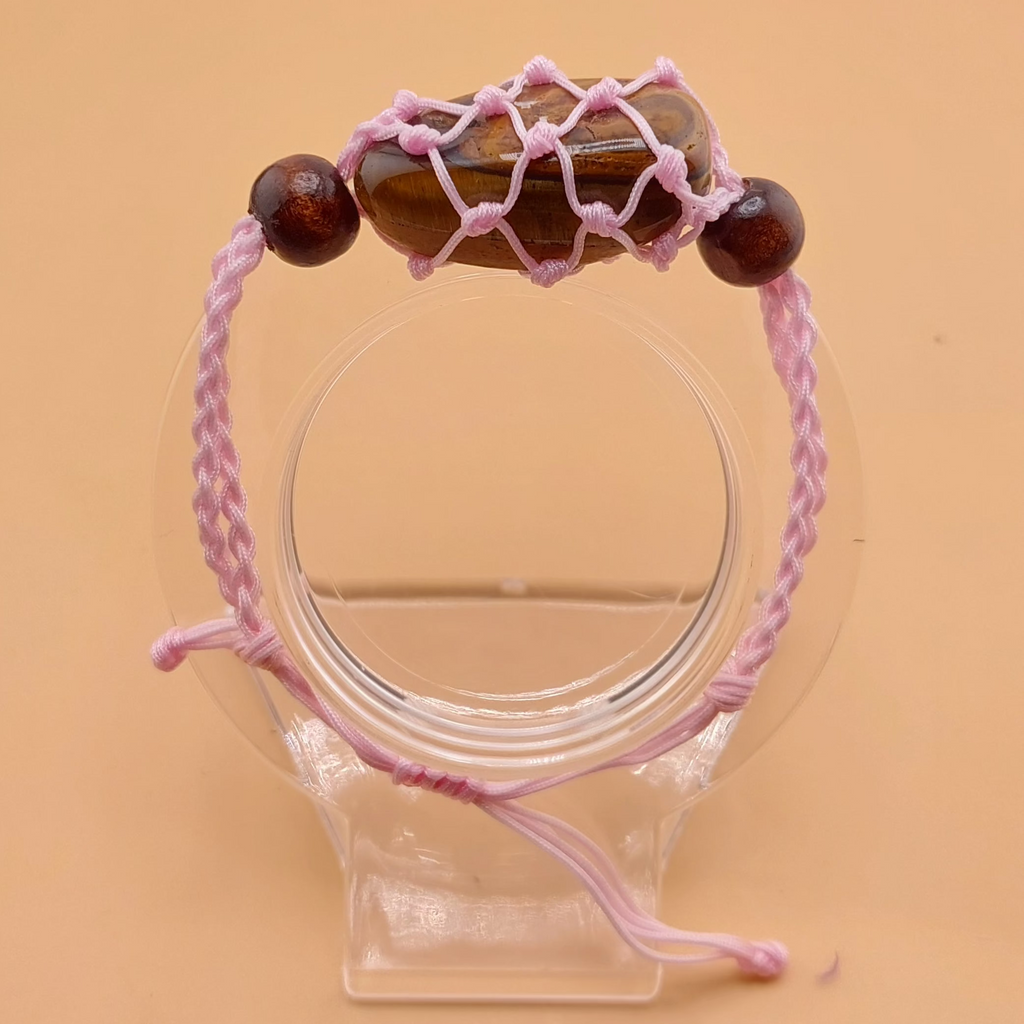 A pink Macrame tumbled stone bracelet displayed on a clear stand against a beige background.