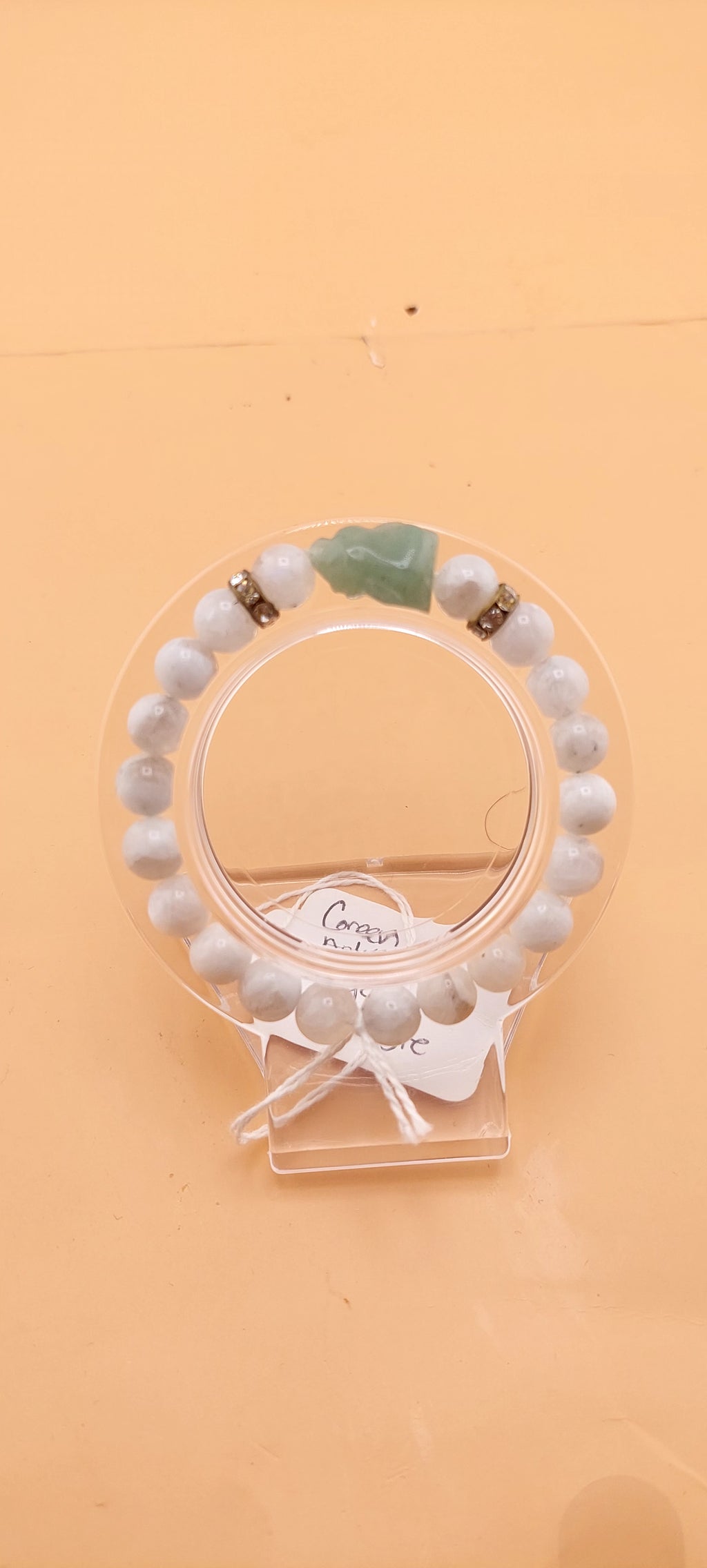A beaded bracelet with green and black colors, presented on a clear stand.