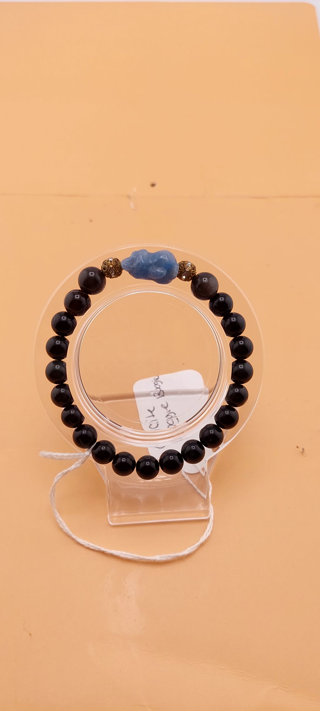 A beaded bracelet with green and black colors, presented on a clear stand.