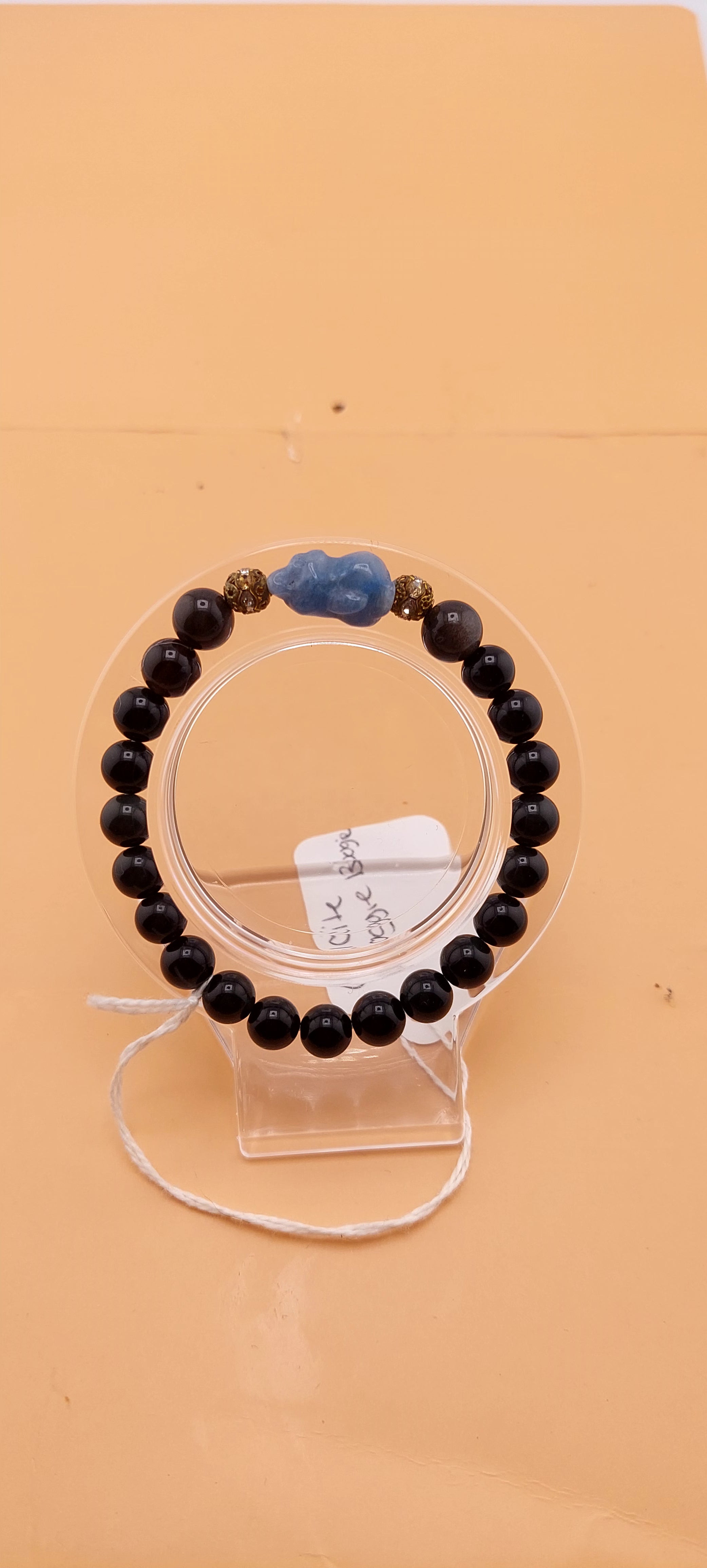 A beaded bracelet with green and black colors, presented on a clear stand.