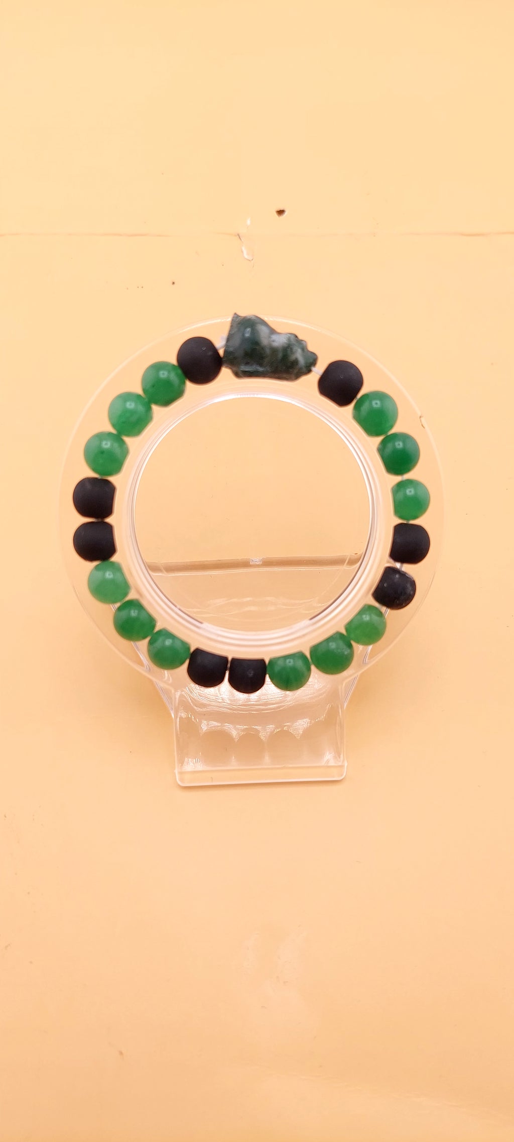 A beaded bracelet with green and black colors, presented on a clear stand.