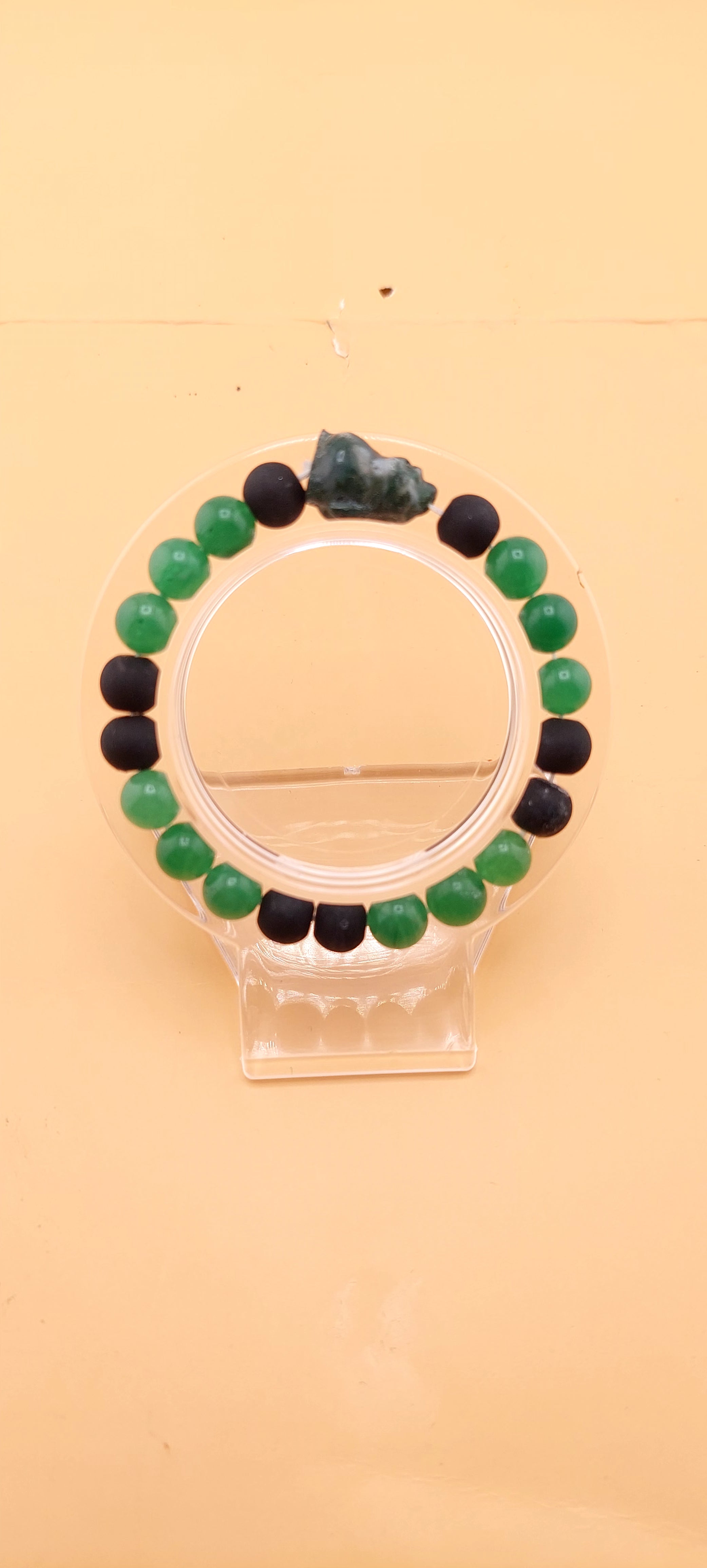 A beaded bracelet with green and black colors, presented on a clear stand.