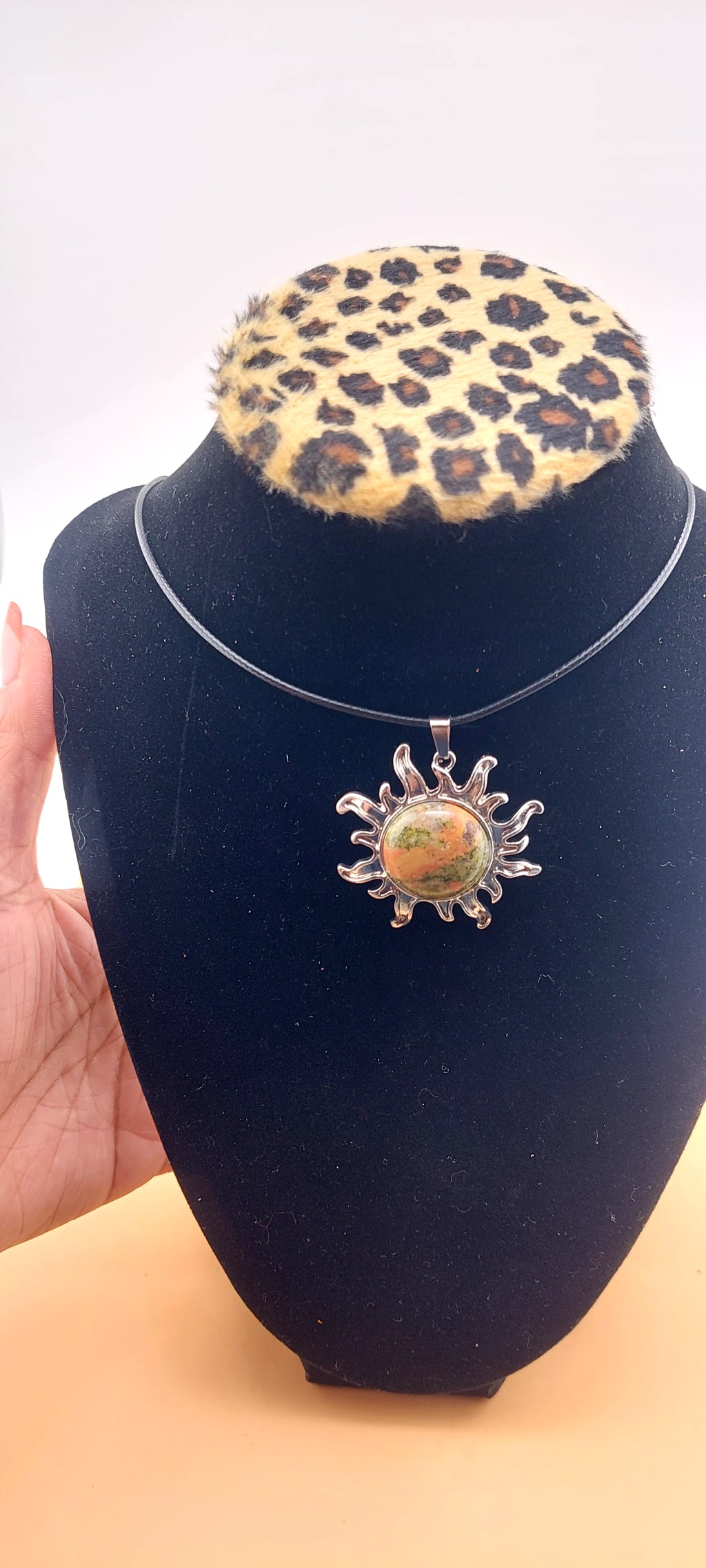 A silver-colored sun-shaped necklace displayed on a black mannequin with a leopard print collar.