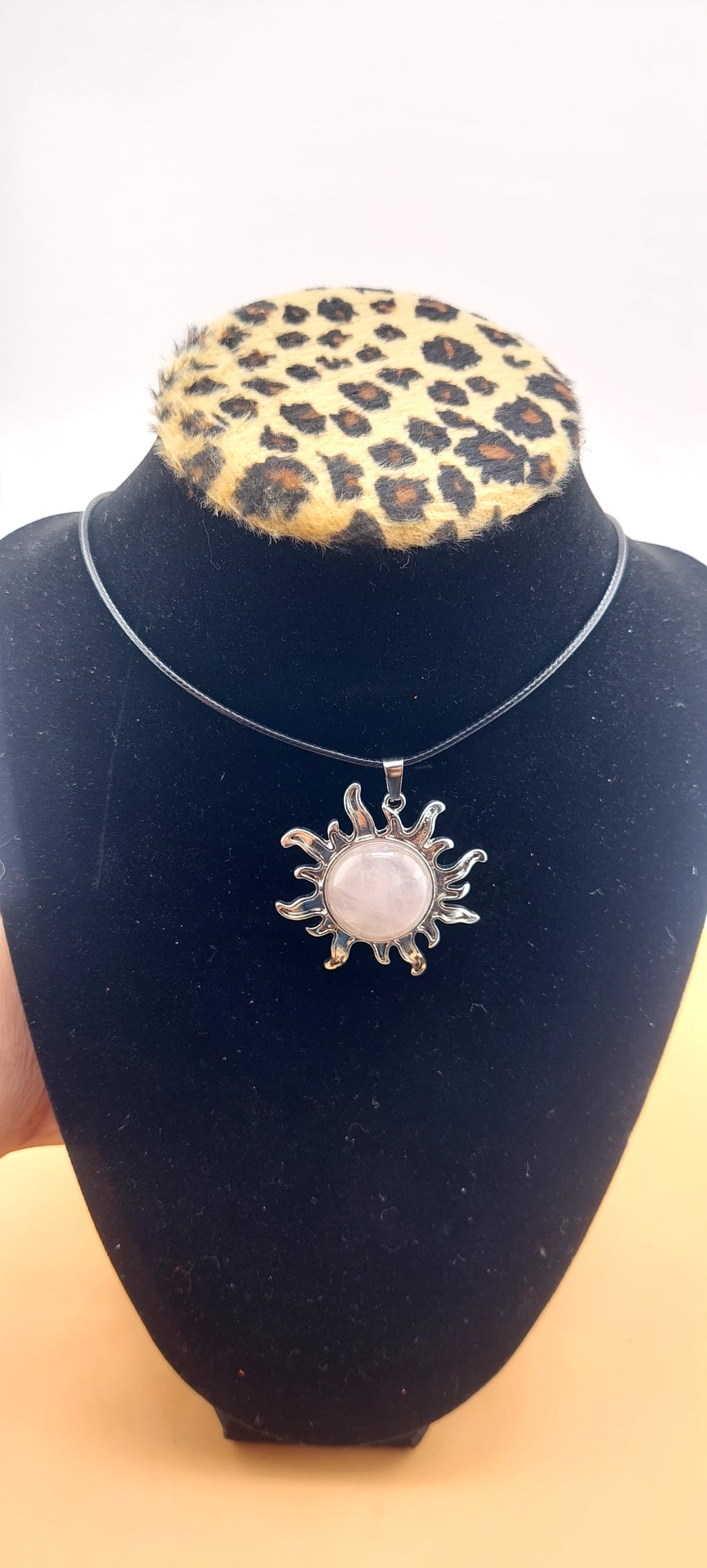 A silver-colored sun-shaped necklace displayed on a black mannequin with a leopard print collar.