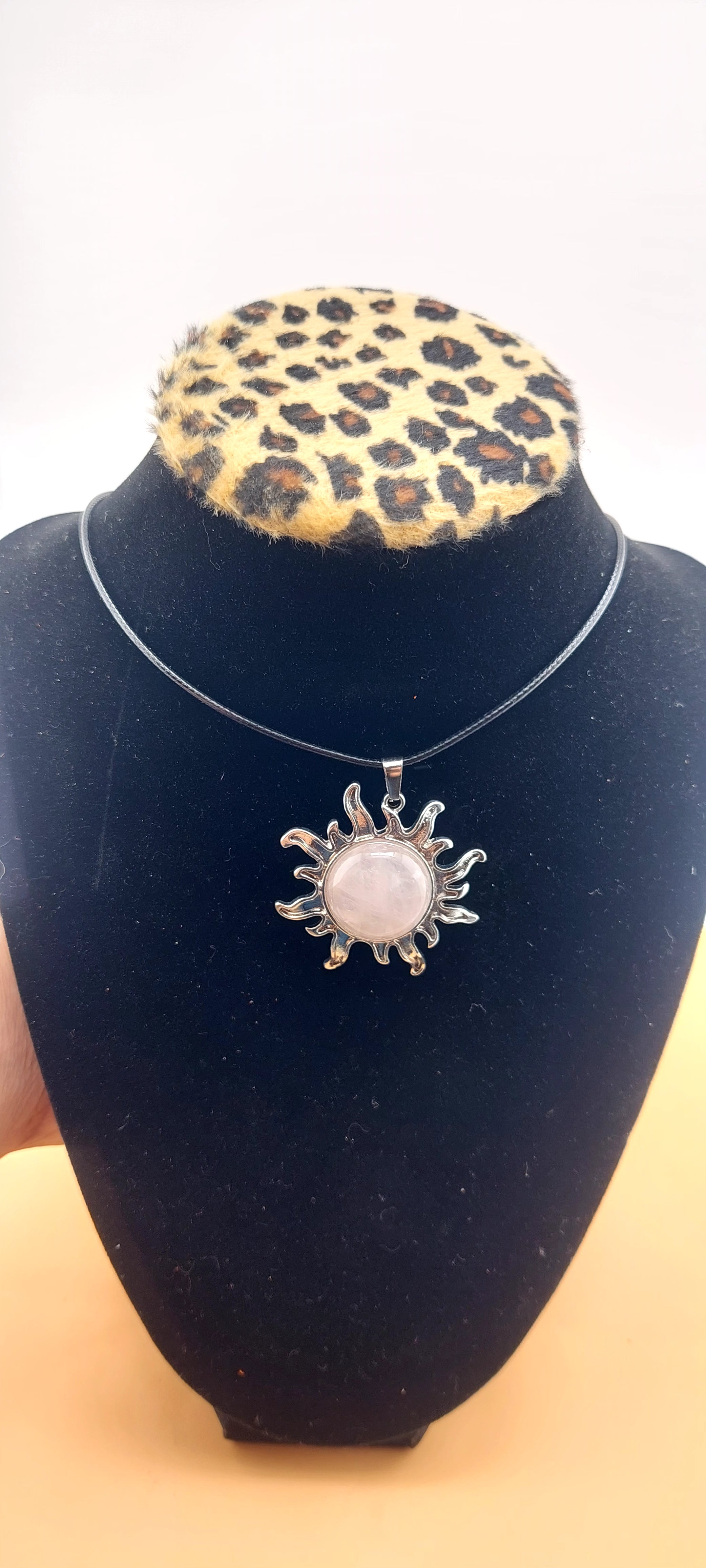 A silver-colored sun-shaped necklace displayed on a black mannequin with a leopard print collar.