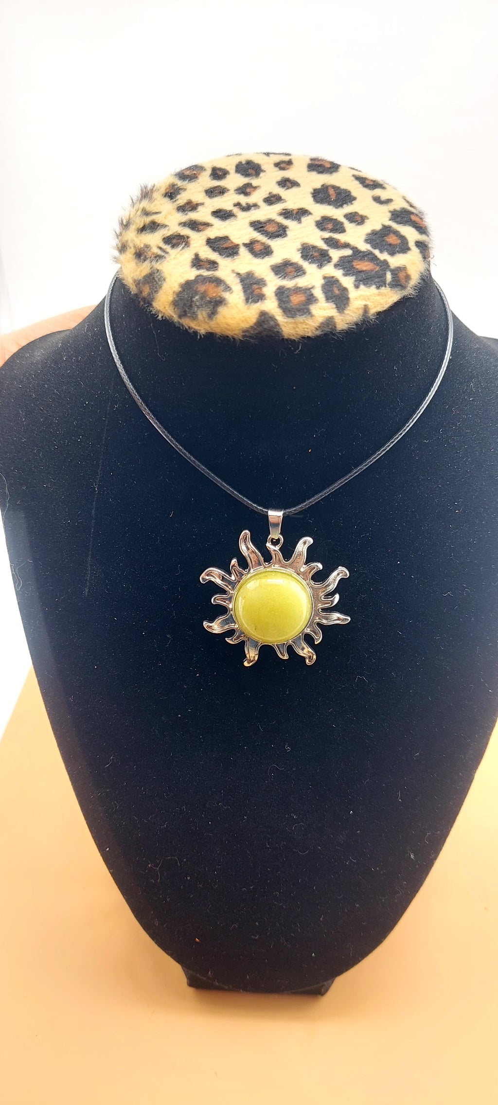 A silver-colored sun-shaped necklace displayed on a black mannequin with a leopard print collar.
