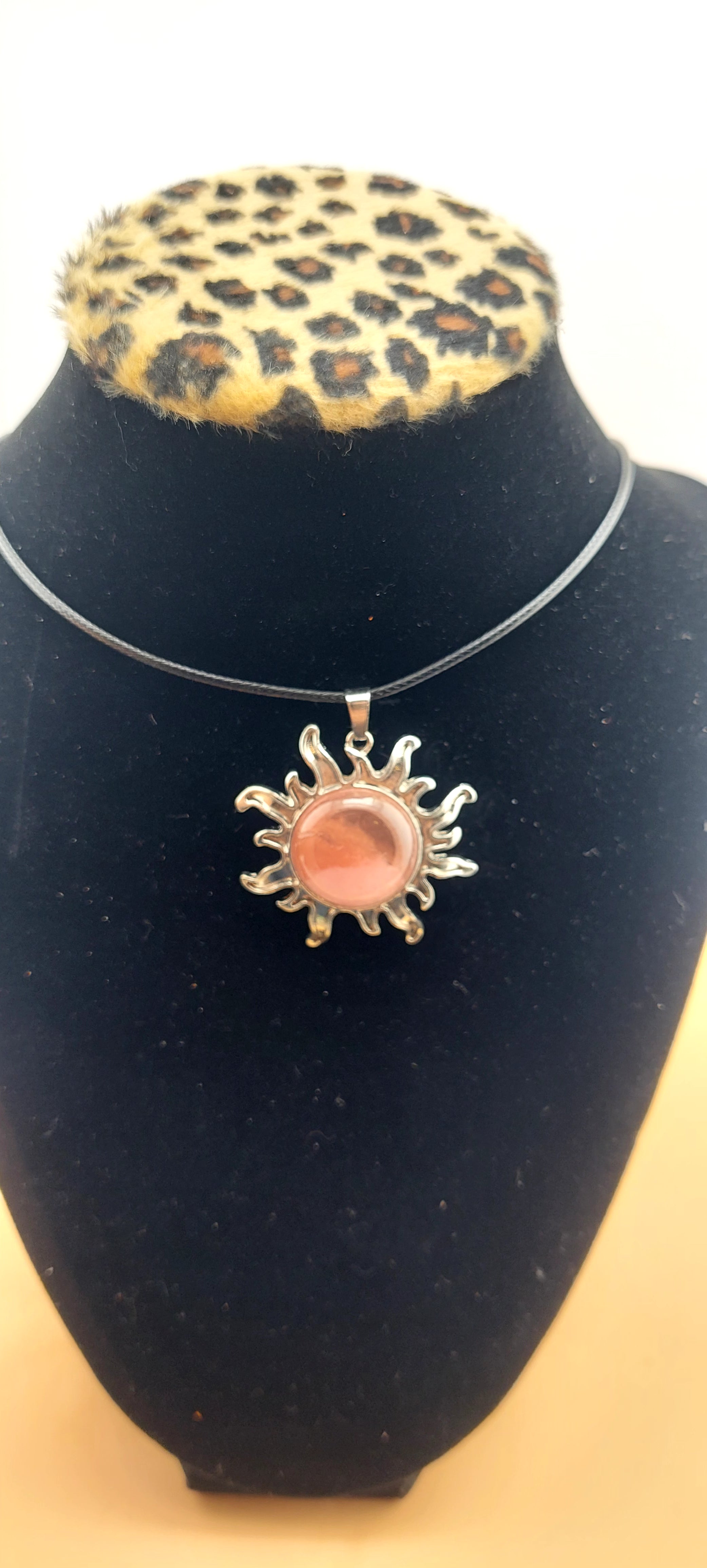 A silver-colored sun-shaped necklace displayed on a black mannequin with a leopard print collar.