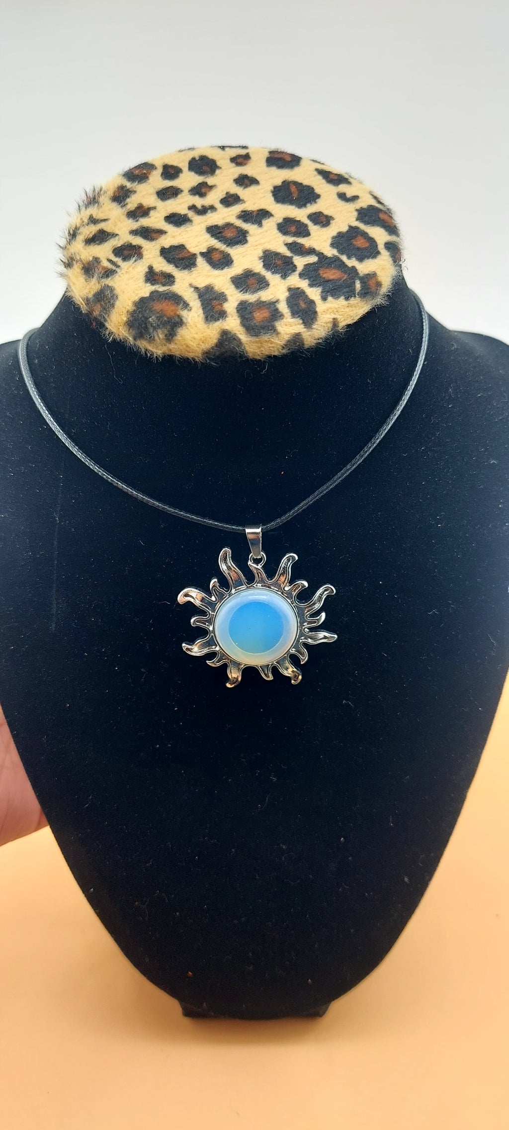 A silver-colored sun-shaped necklace displayed on a black mannequin with a leopard print collar.