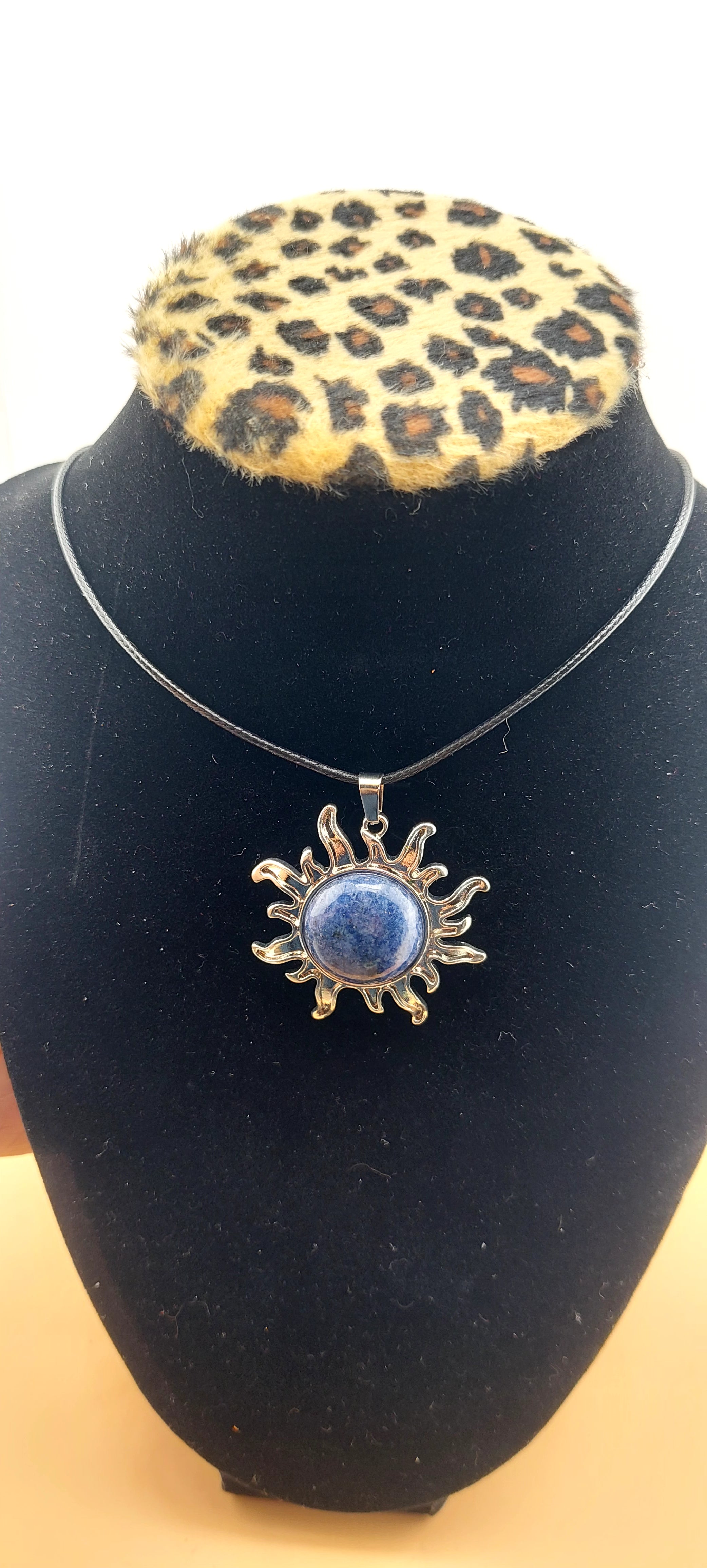 A silver-colored sun-shaped necklace displayed on a black mannequin with a leopard print collar.