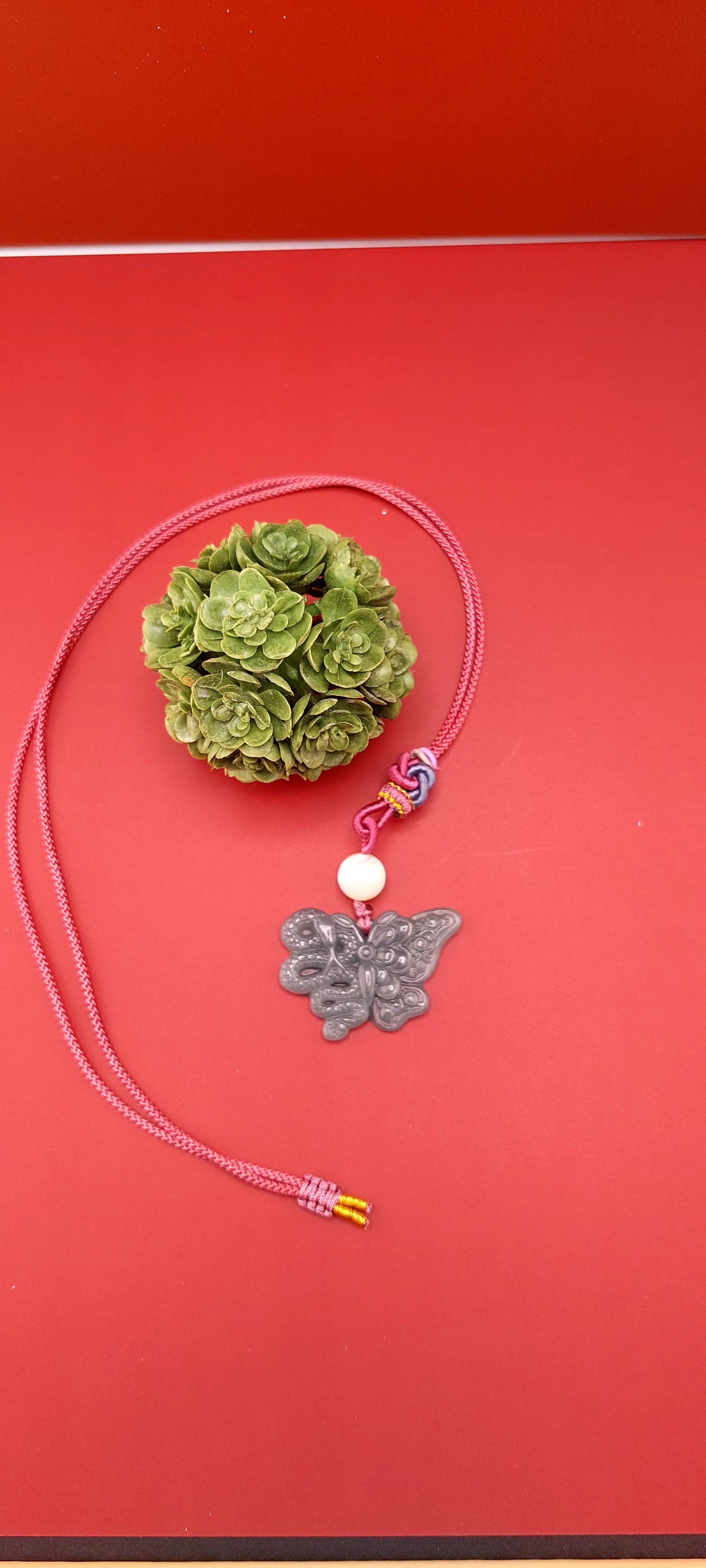 A blue water jade necklace with a snake and butterfly design, displayed against a red background.