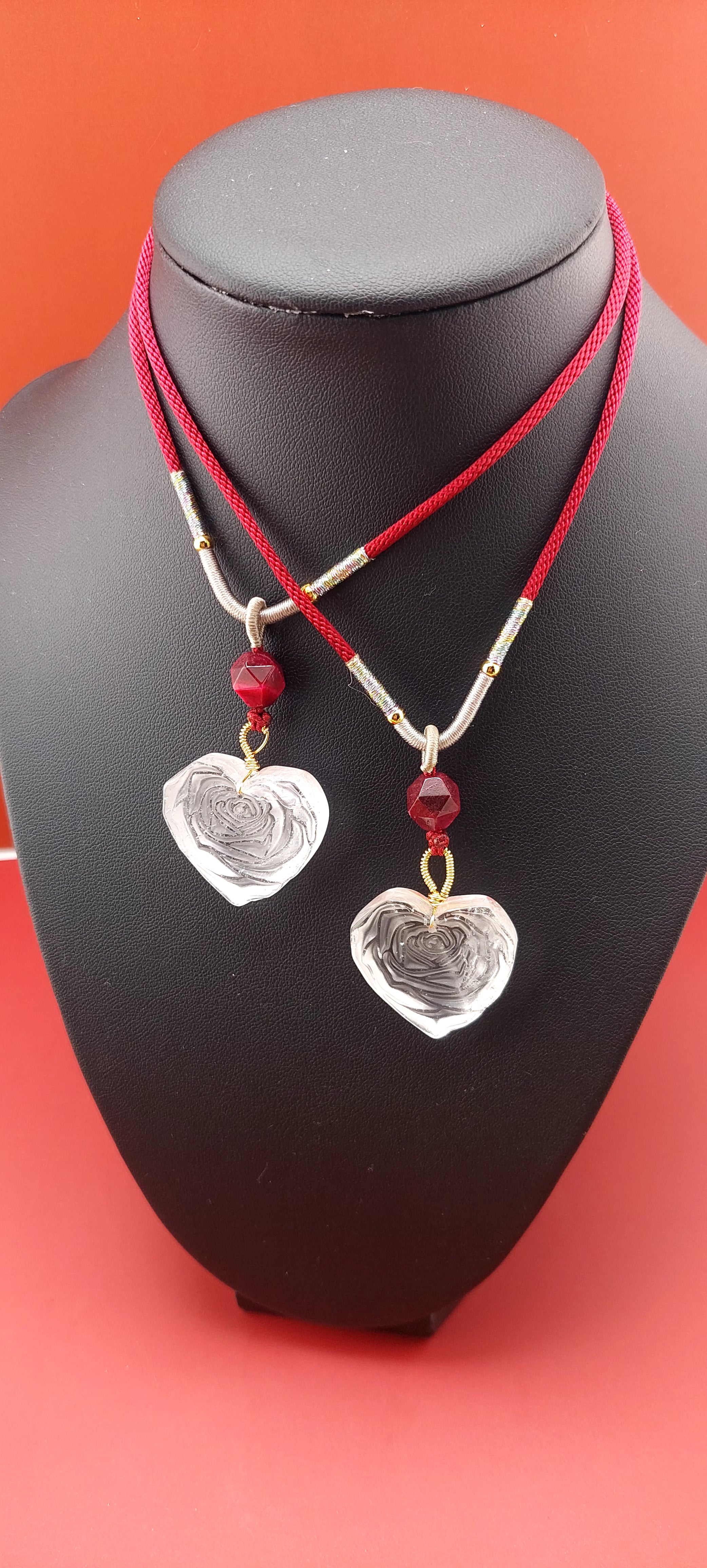 A clear quartz rose heart necklace with a red and white threaded chain and silver-colored hearts.