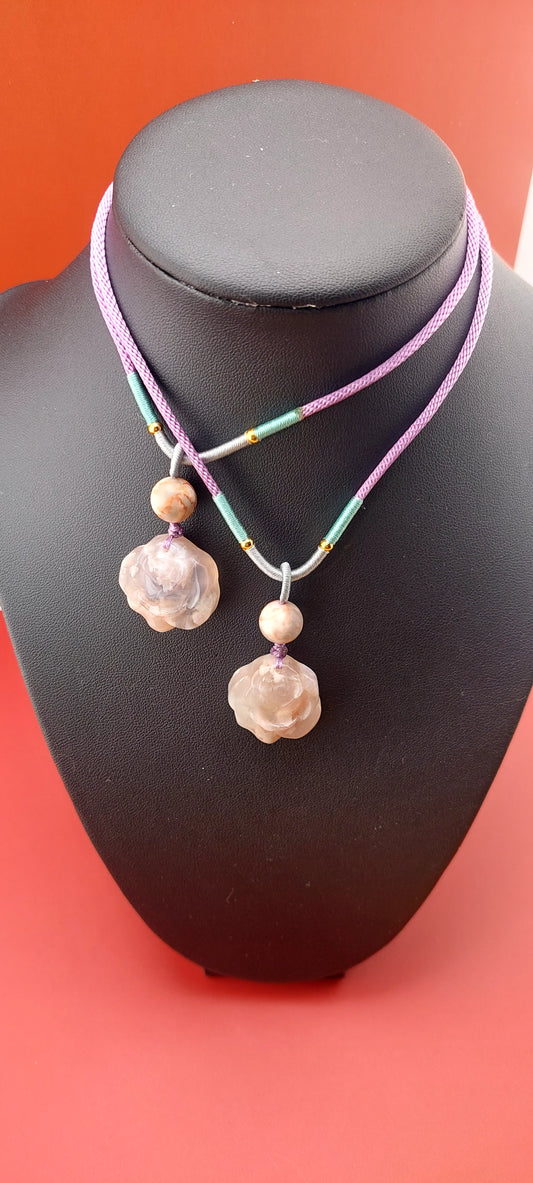 A rose flower agate necklace displayed on a mannequin with a silver chain and pink and green beaded cord.