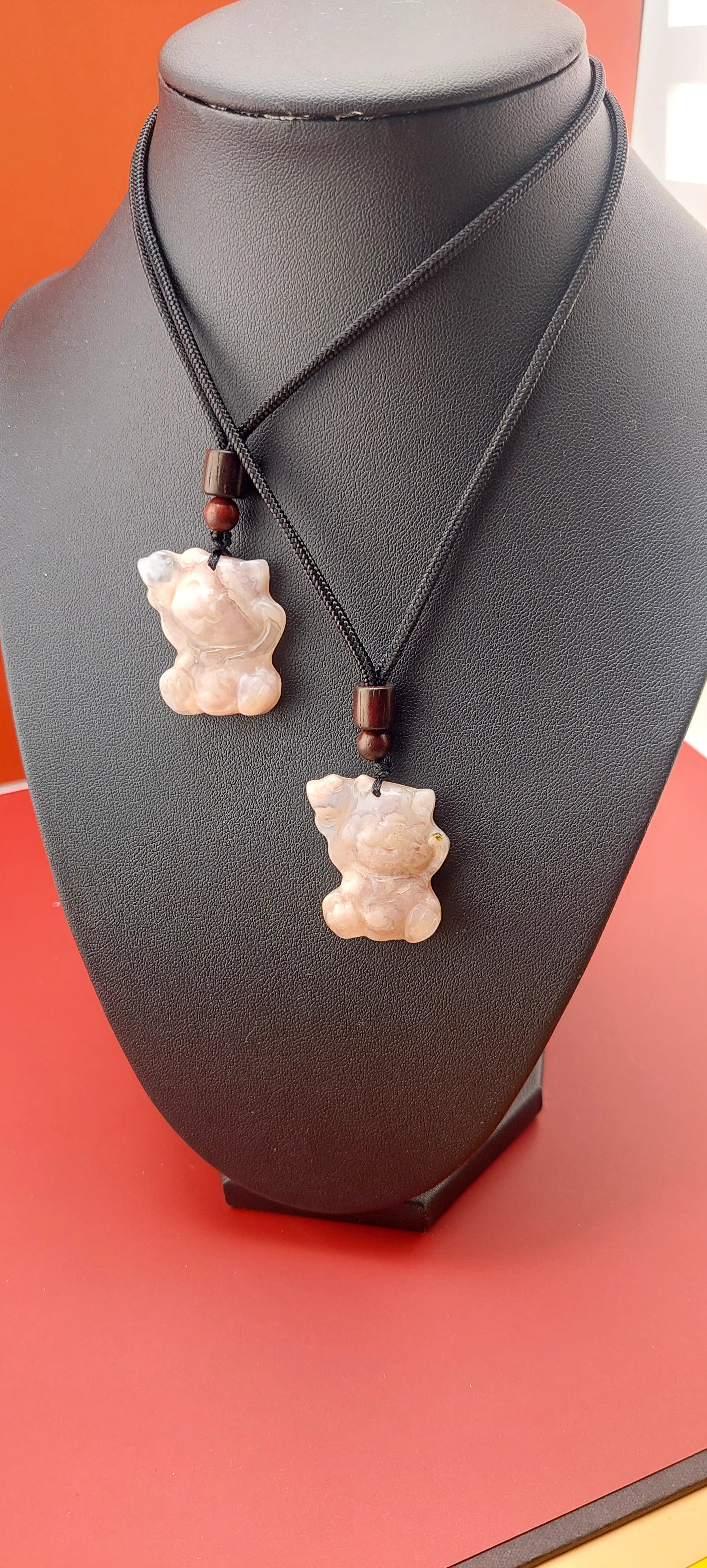 A necklace with a flower agate stone pendant, shaped like a cat, displayed on a black mannequin against a red background.