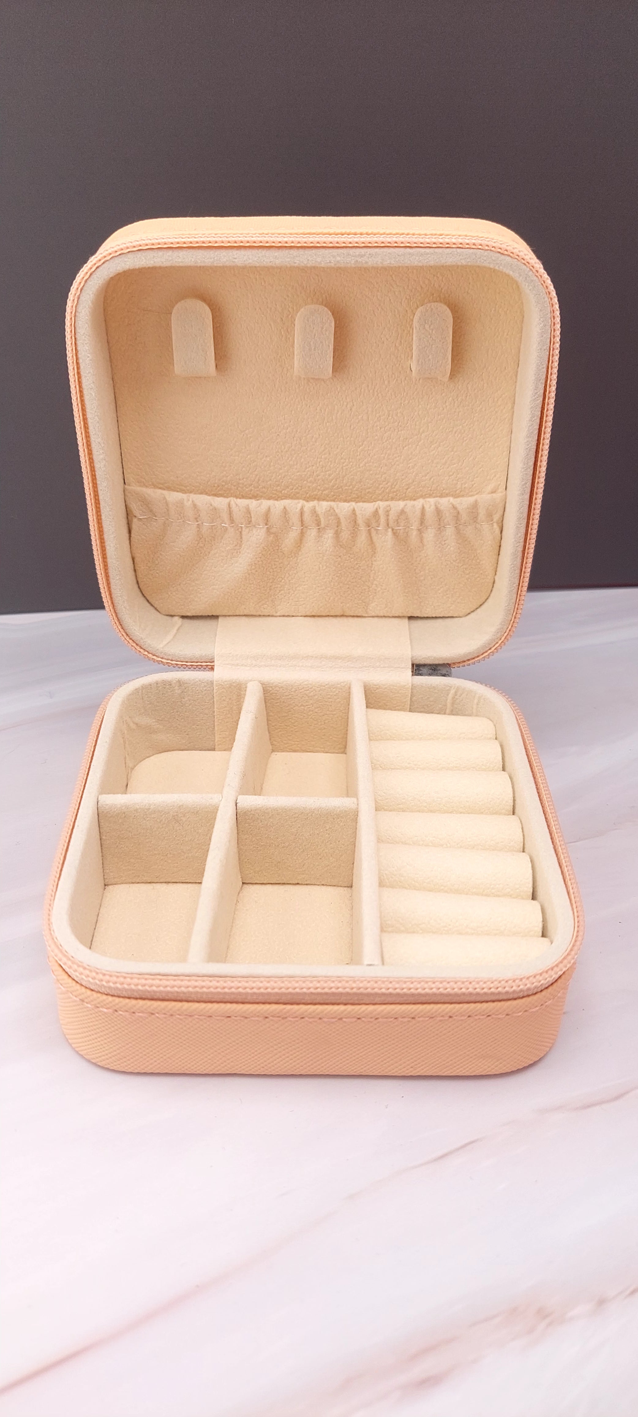 A square jewelry box made of beige material with a beige interior, featuring compartments for organizing jewelry.