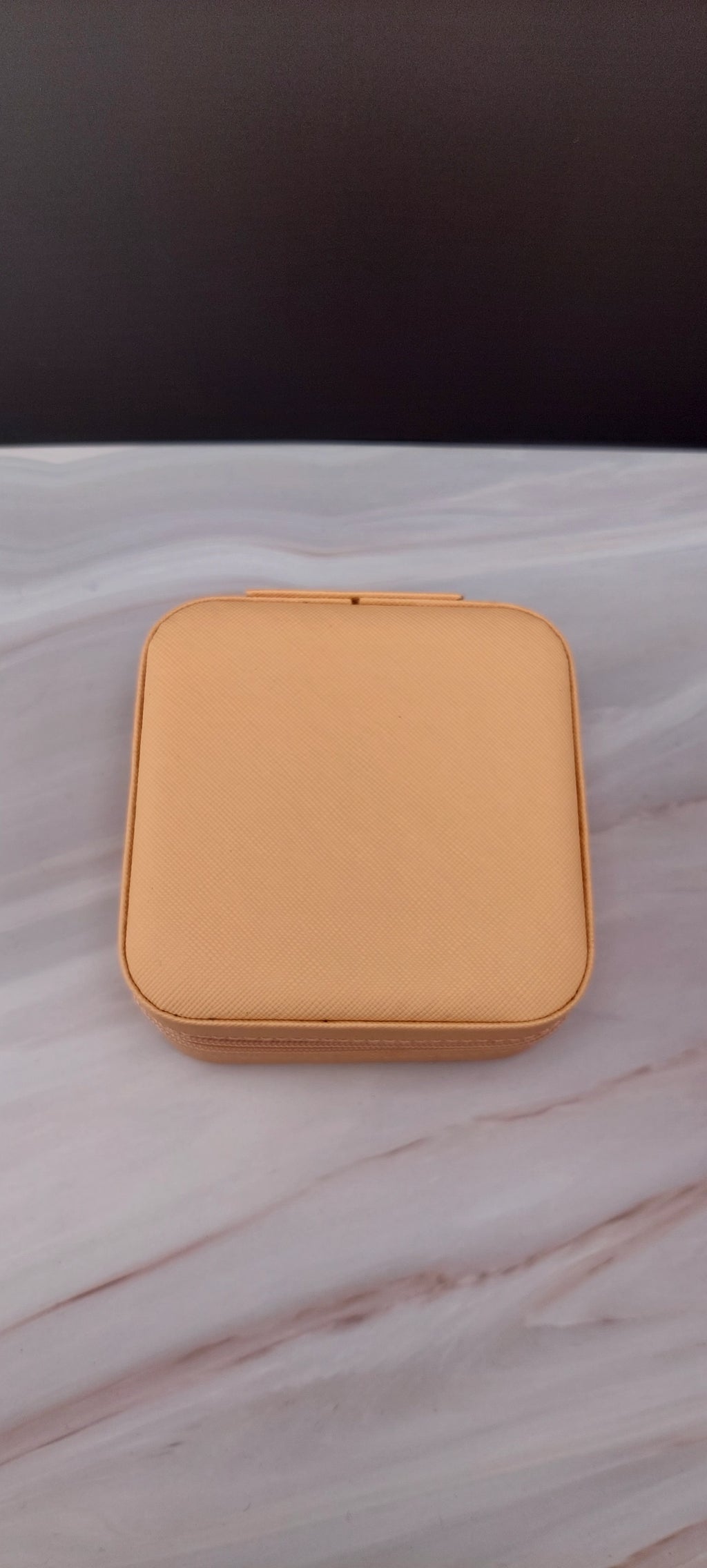 A square jewelry box made of beige material with a beige interior, featuring compartments for organizing jewelry.
