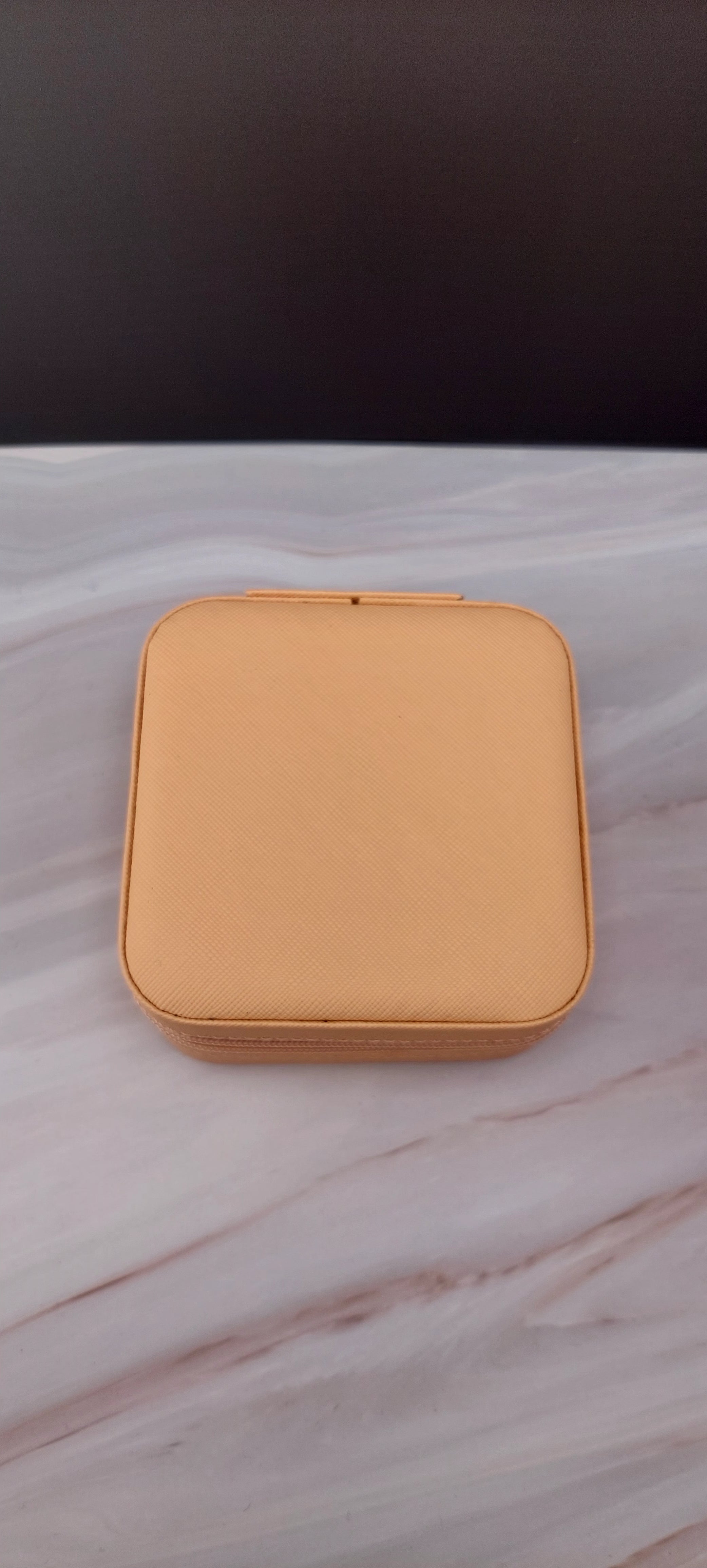 A square jewelry box made of beige material with a beige interior, featuring compartments for organizing jewelry.