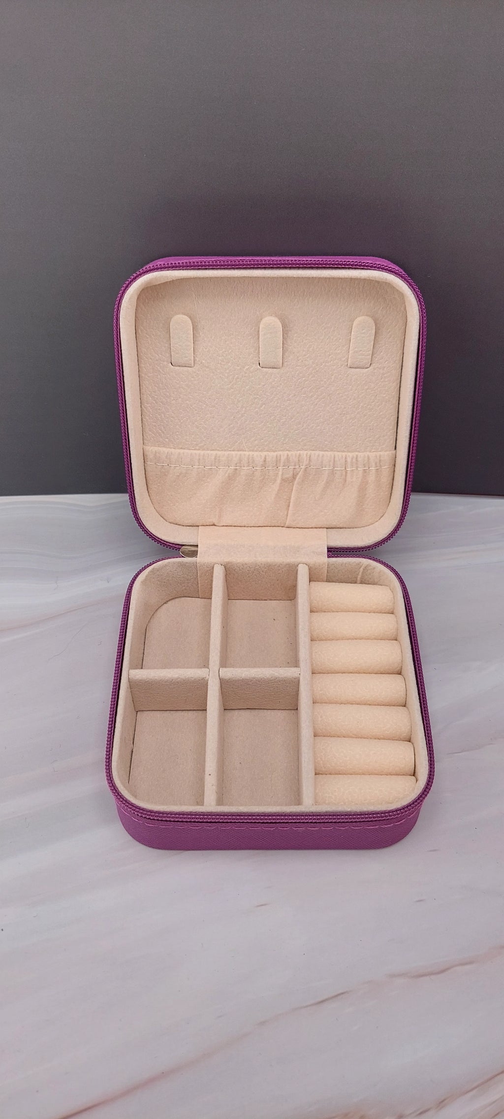 A square jewelry box made of purple material with a beige interior, featuring compartments for organizing jewelry.