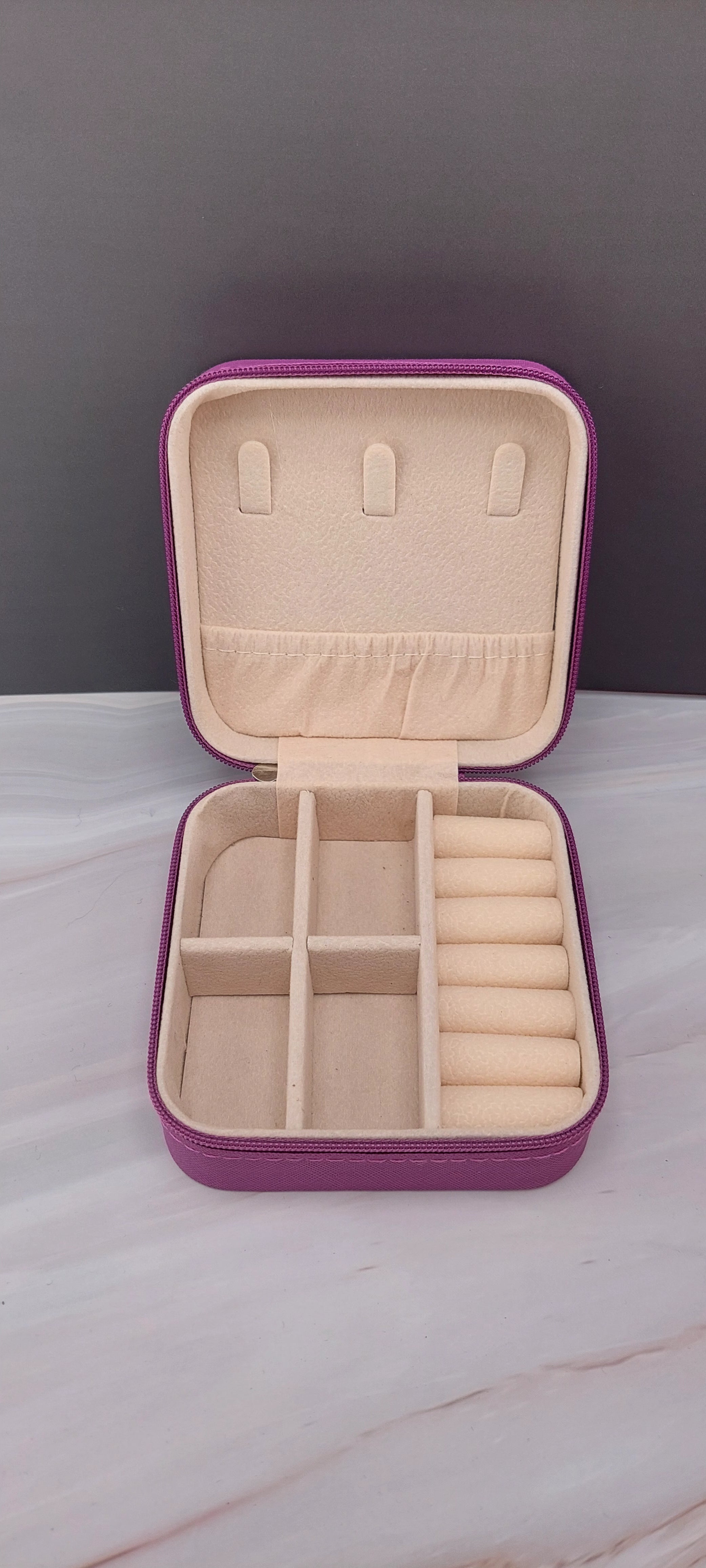 A square jewelry box made of purple material with a beige interior, featuring compartments for organizing jewelry.