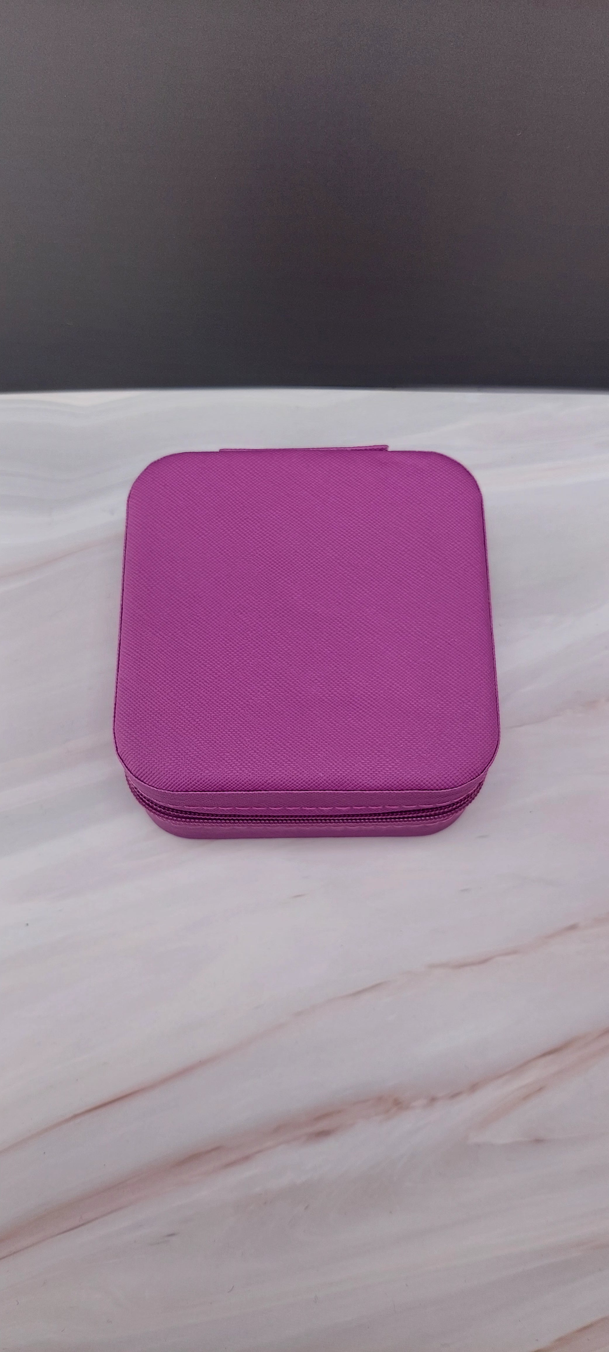 A square jewelry box made of  purple material with a beige interior, featuring compartments for organizing jewelry.