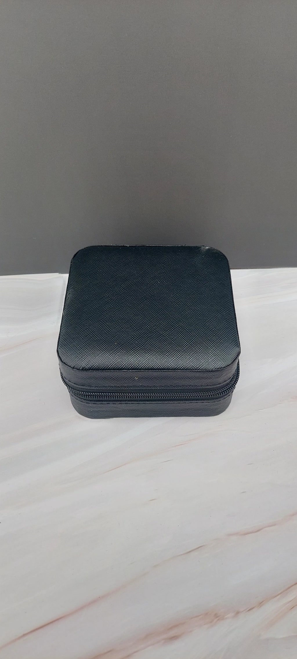 A square jewelry box made of black material with a beige interior, featuring compartments for organizing jewelry.