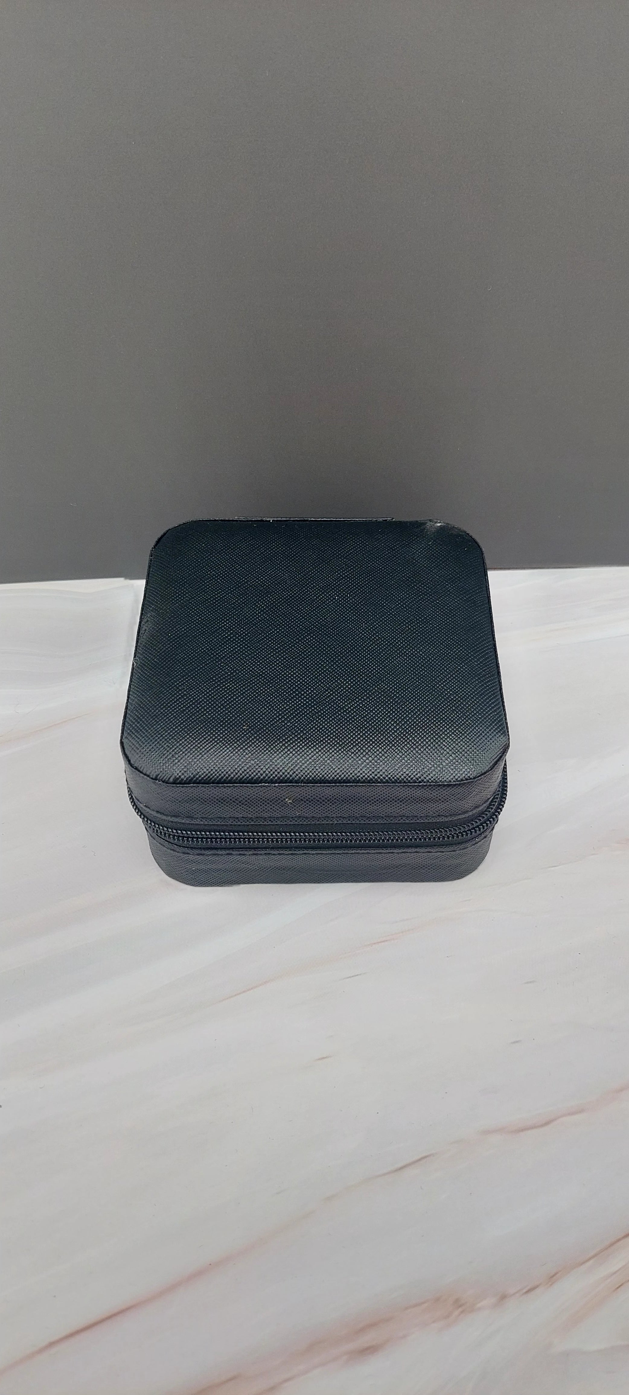 A square jewelry box made of black material with a beige interior, featuring compartments for organizing jewelry.