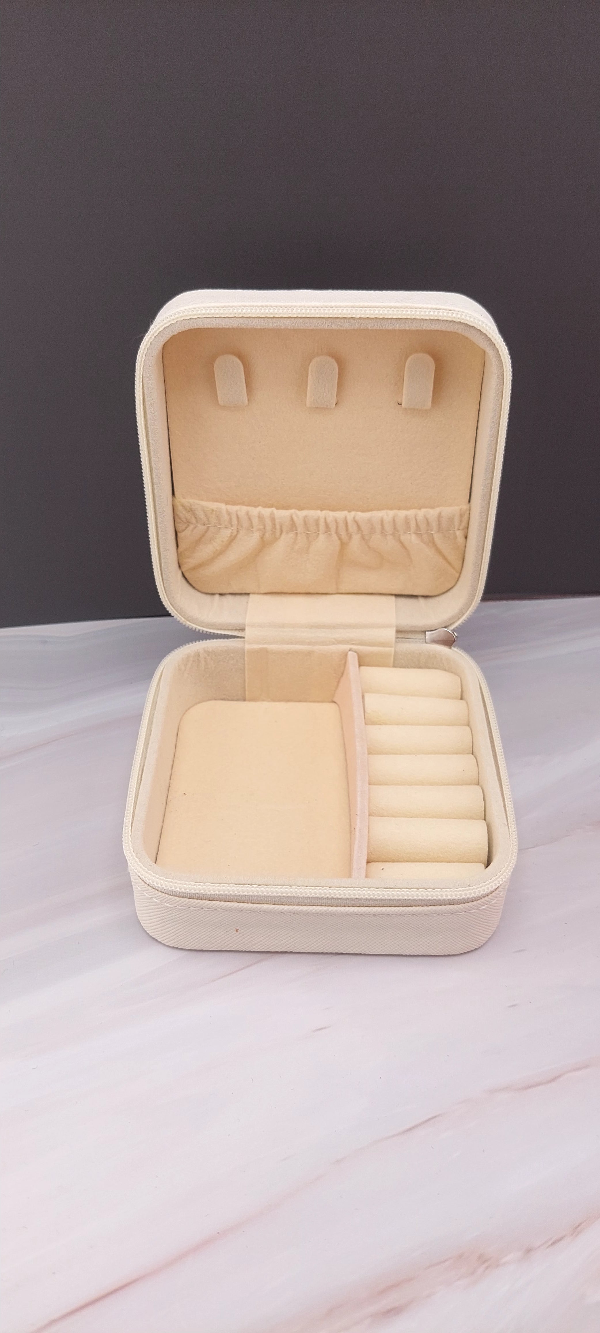 A square jewelry box made of white material with a beige interior, featuring compartments for organizing jewelry.