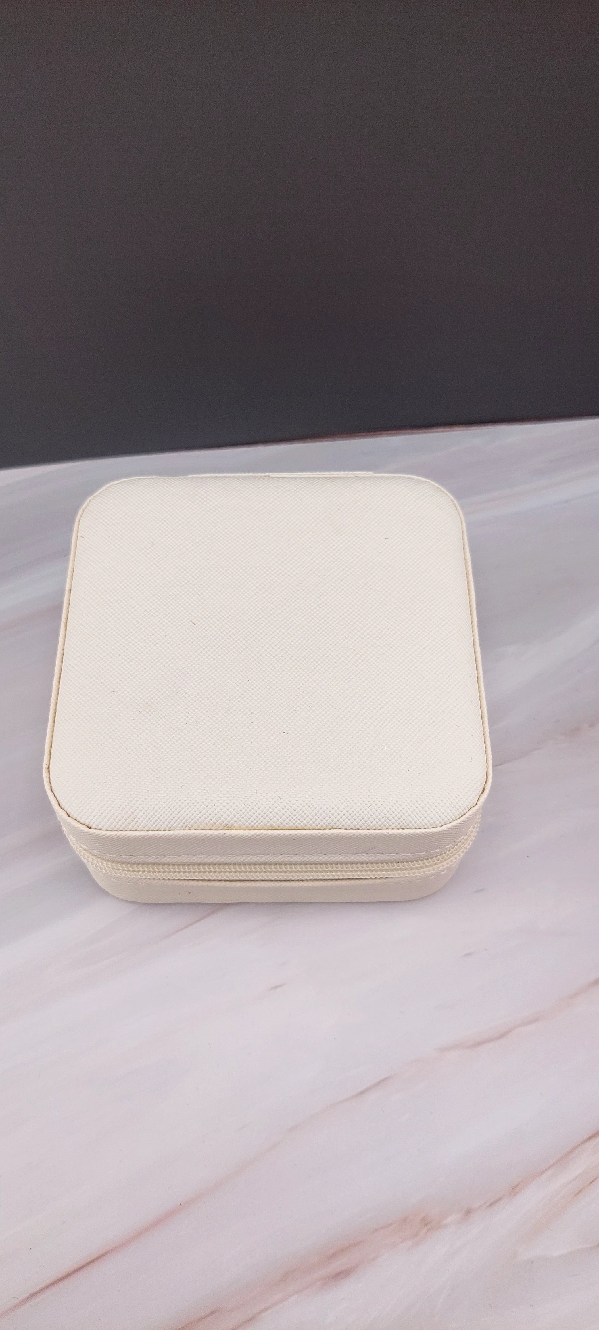 A square jewelry box made of white material with a beige interior, featuring compartments for organizing jewelry.